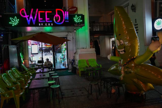 <p>A tourist sits outside a cannabis shop in Bangkok, Thailand</p>