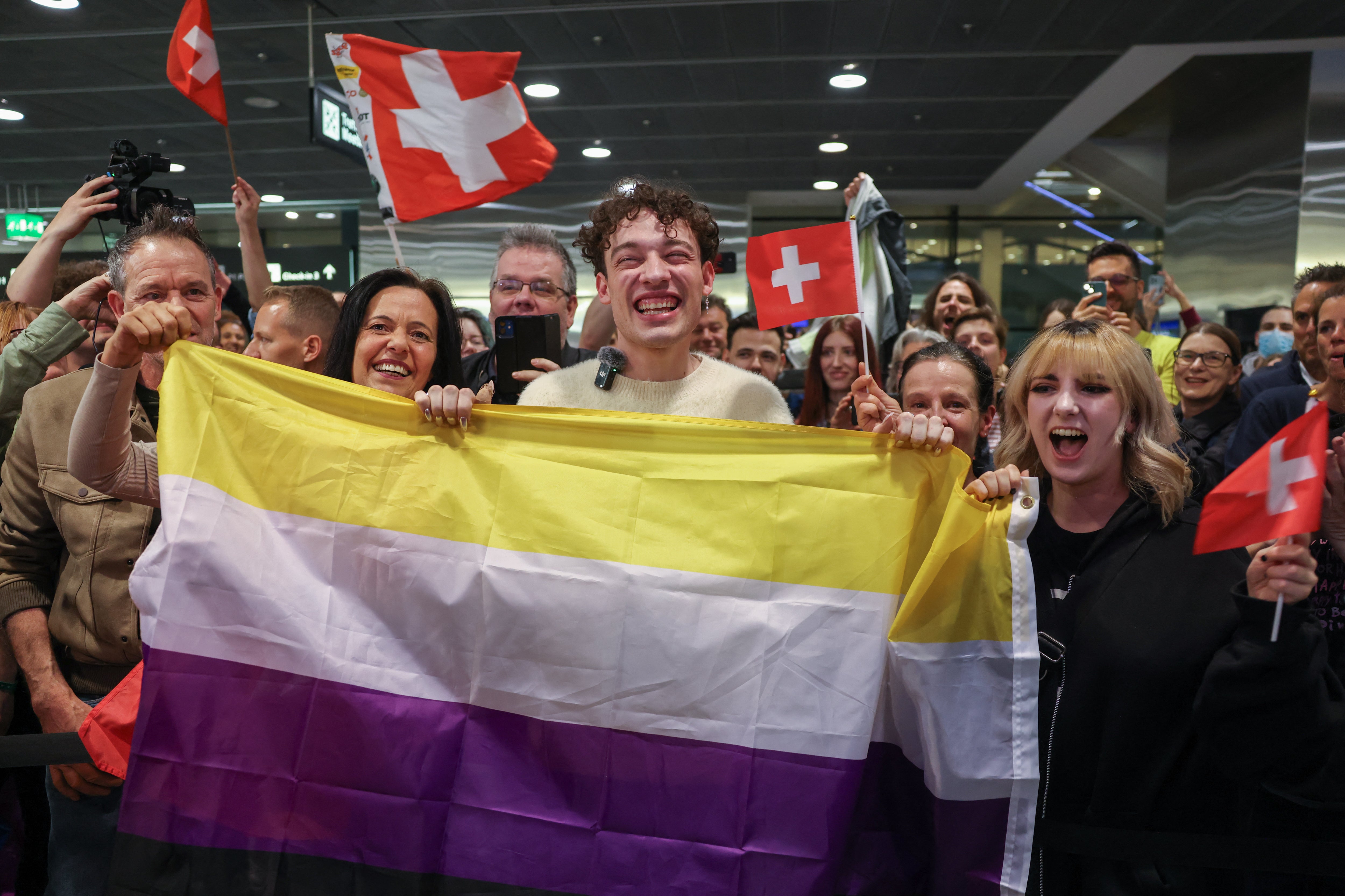 Nemo holding the non-binary flag with supporters at Zurich airport following their Eurovision win