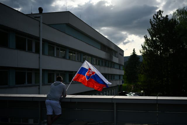 <p>A man waves Slovakia’s flag outside the hospital in Banska Bystrica where Robert Fico is being treated</p>