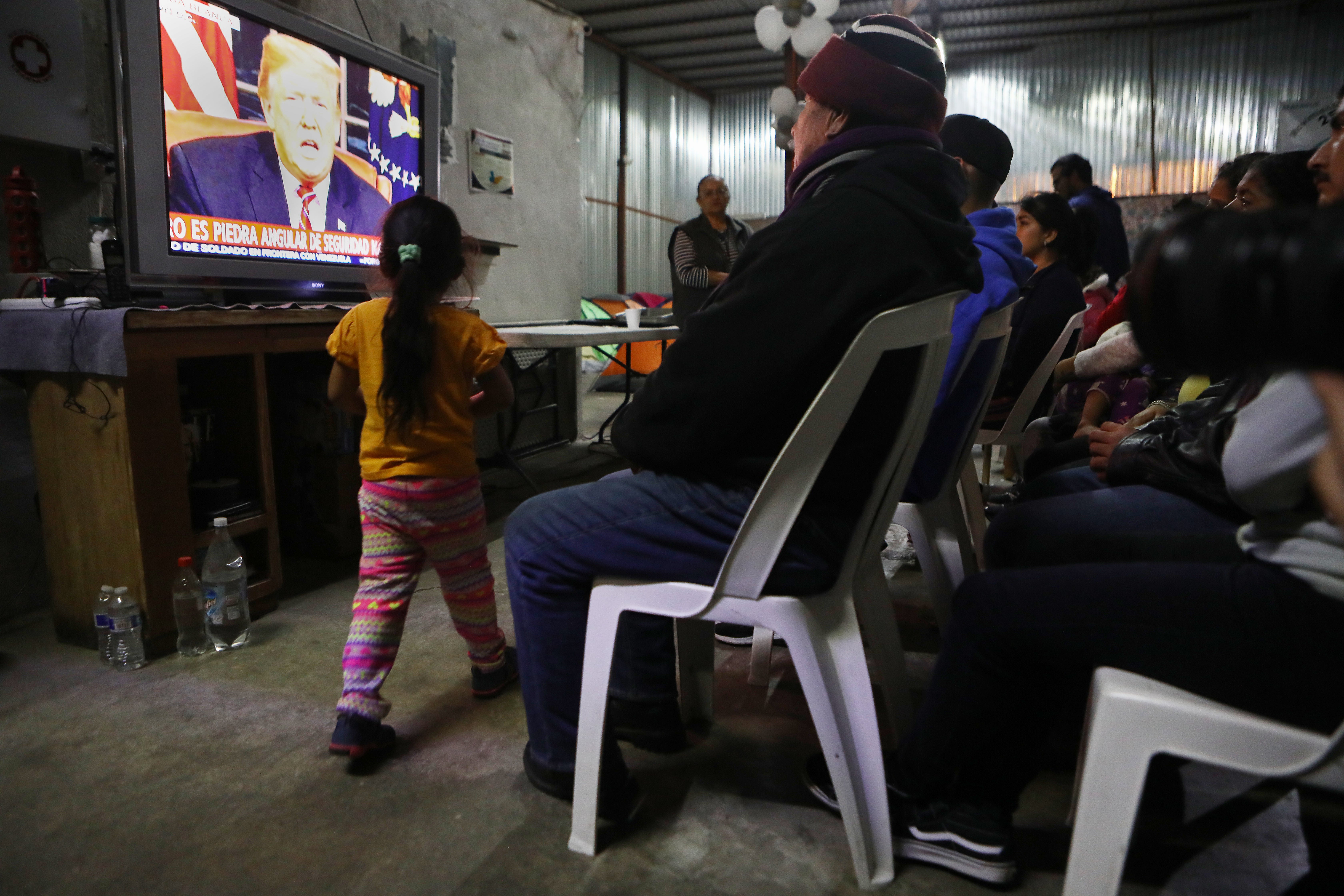 Migrants view a live televised speech by President Donald Trump on border security at a shelter for migrants on January 8, 2019 in Tijuana, Mexico