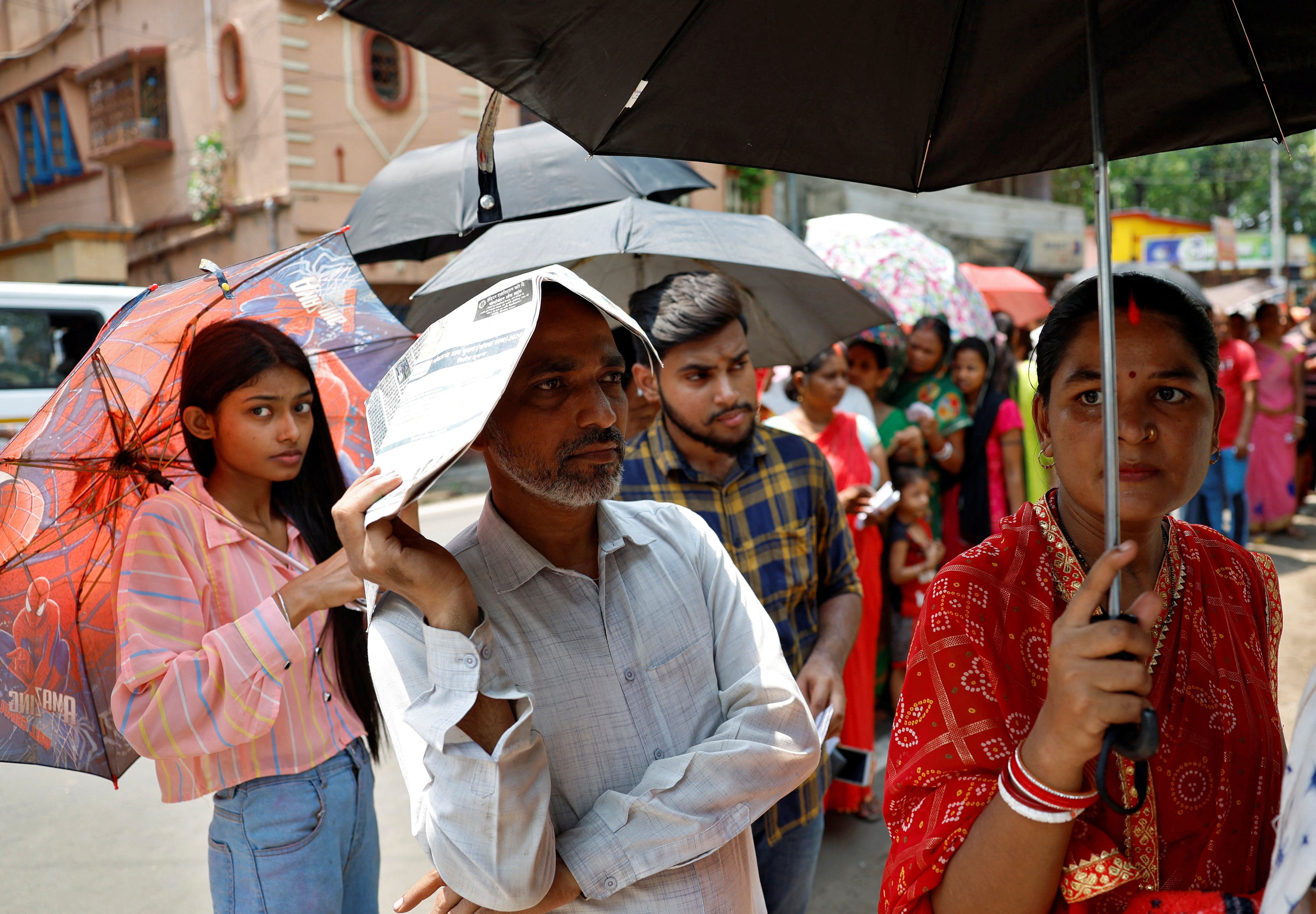 A man uses a newspaper as others use umbrellas to protect themselves from the heat as they wait to vote