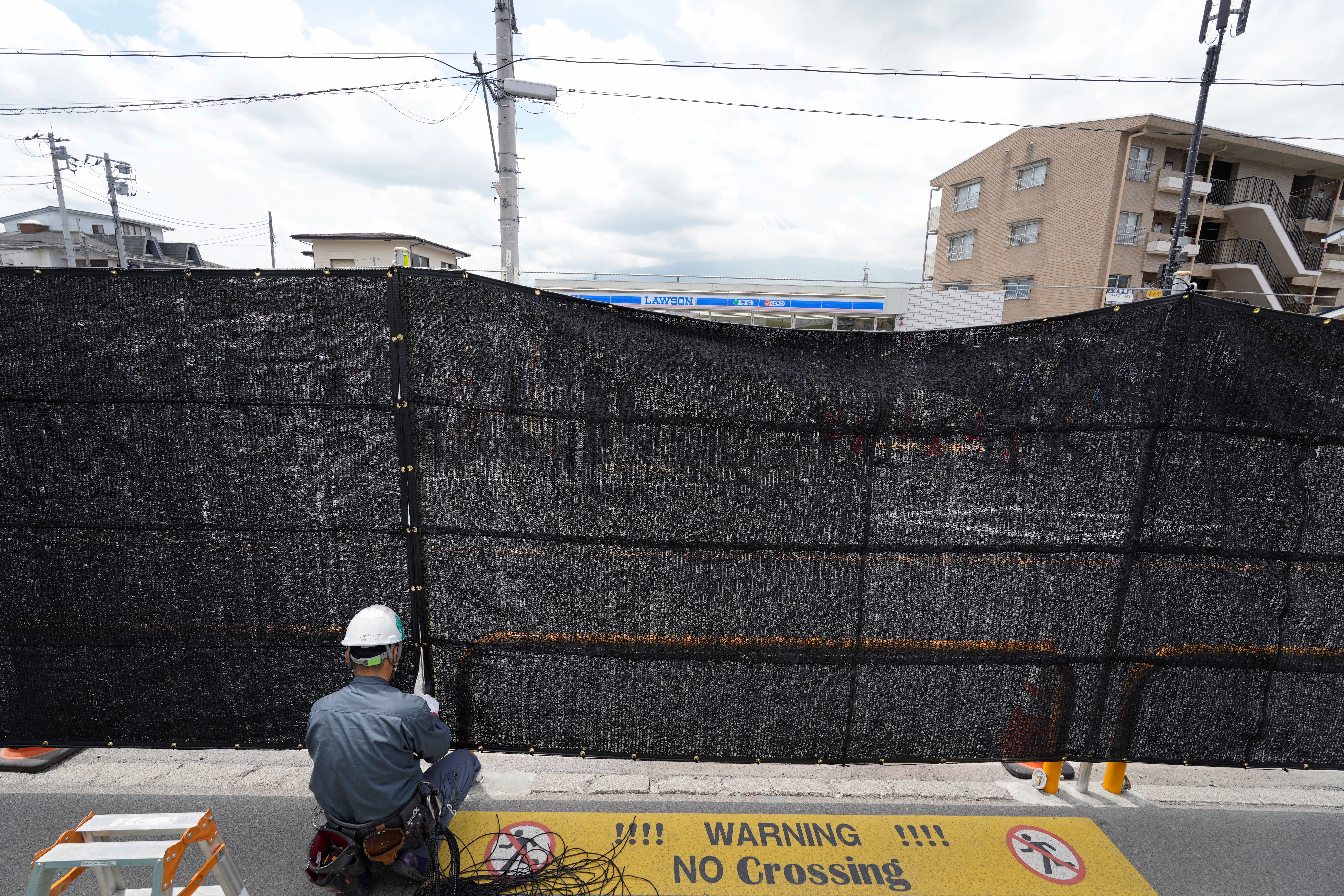 A worker installs a black shading net on the opposite side of the Lawson Kawaguchiko Ekimae convenience store in Fujikawaguchiko