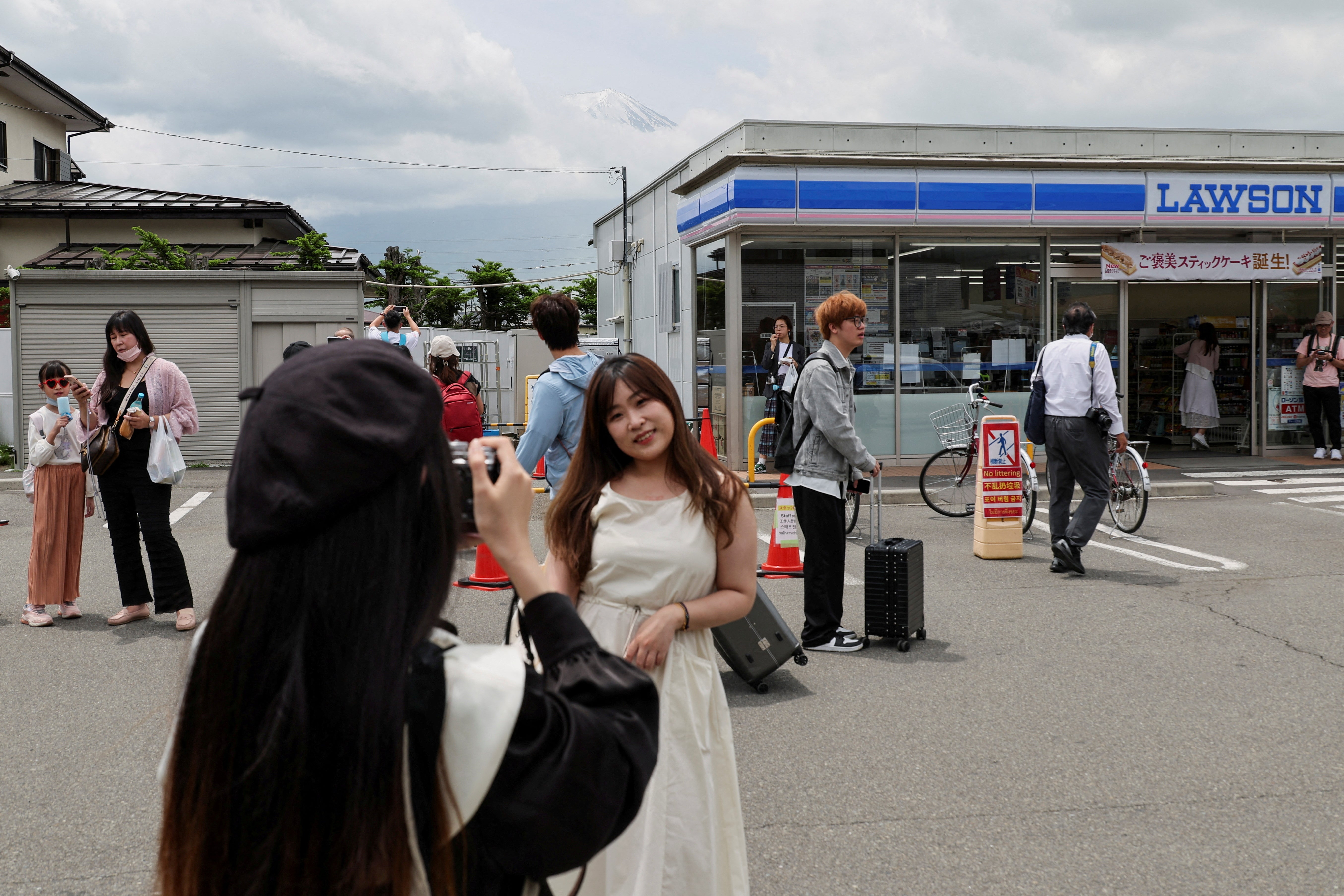 A tourist poses for a photo of Mount Fuji appearing over a convenience store after a barrier to block the popular tourist spot was installed, in Fujikawaguchiko
