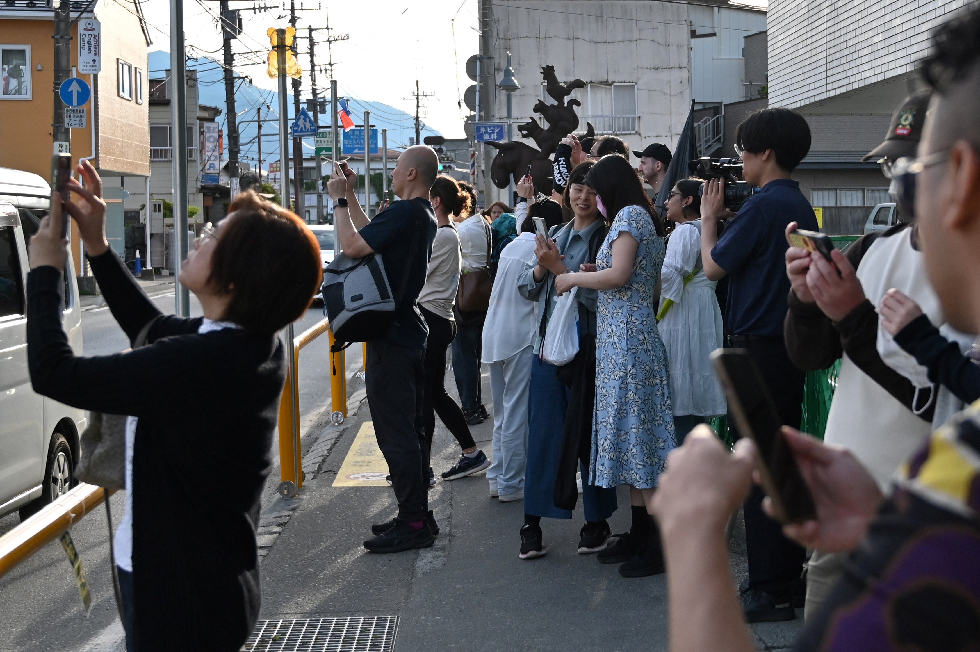 Tourists crowding the pavement to take pictures of Mount Fuji from opposite a convenience store in the town of Fujikawaguchiko
