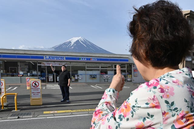 <p>Una persona toma fotos del monte Fuji al frente de una tienda, horas antes de la instalación de una red para bloquear la vista del volcán</p>