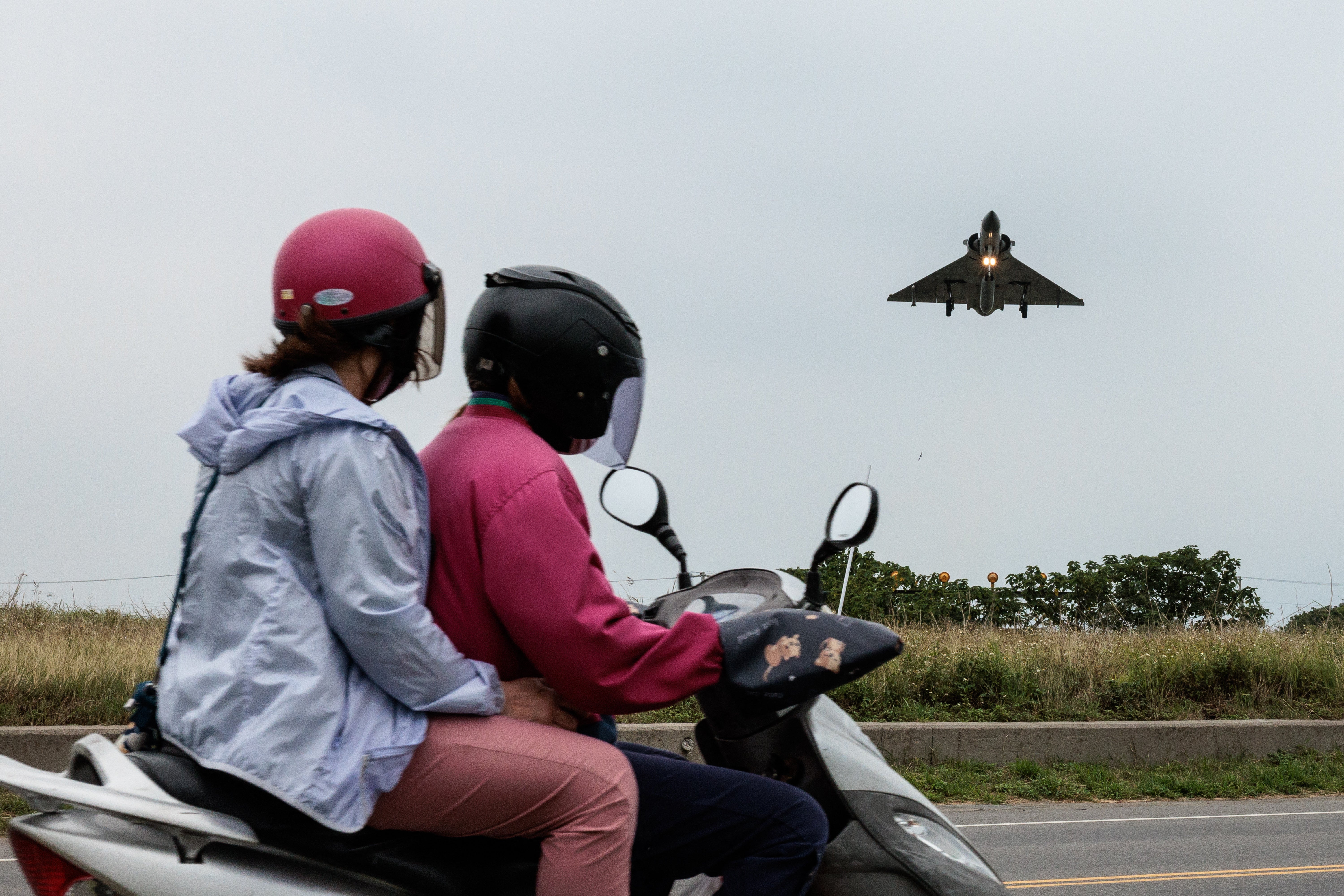 Two people ride a motorcycle as a Taiwanese Air Force Mirage 2000 fighter jet approaches for landing at an air force base in Hsinchu in northern Taiwan on 23 May 2024