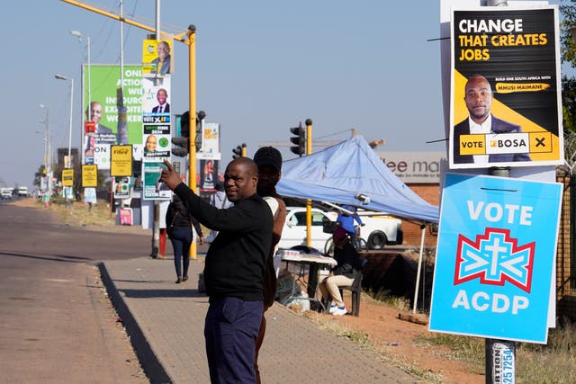 <p>A man waits for a taxi along a street lined with election posters in the Hammanskraal township, Pretoria</p>