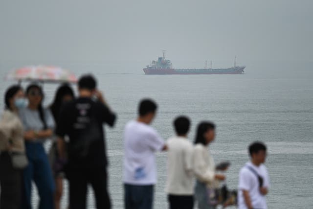 <p>Tourists look on as a coastal freighter sails past a tourist spot called “68 Nautical Miles” on Pingtan island, the closest point in China to Taiwan’s main island, in southeast China’s Fujian province</p>