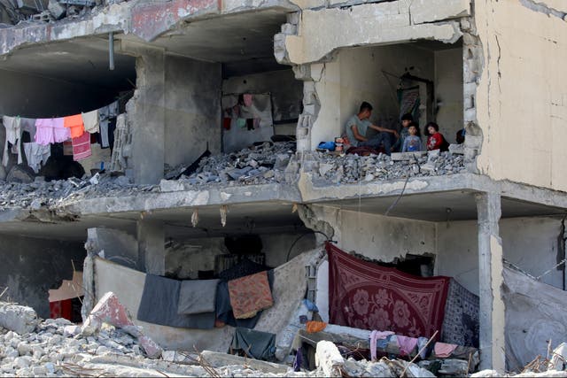<p>A Palestinian man and his children sit in a destroyed room following the targeting of a residential building by an Israeli airstrike in Rafah</p>