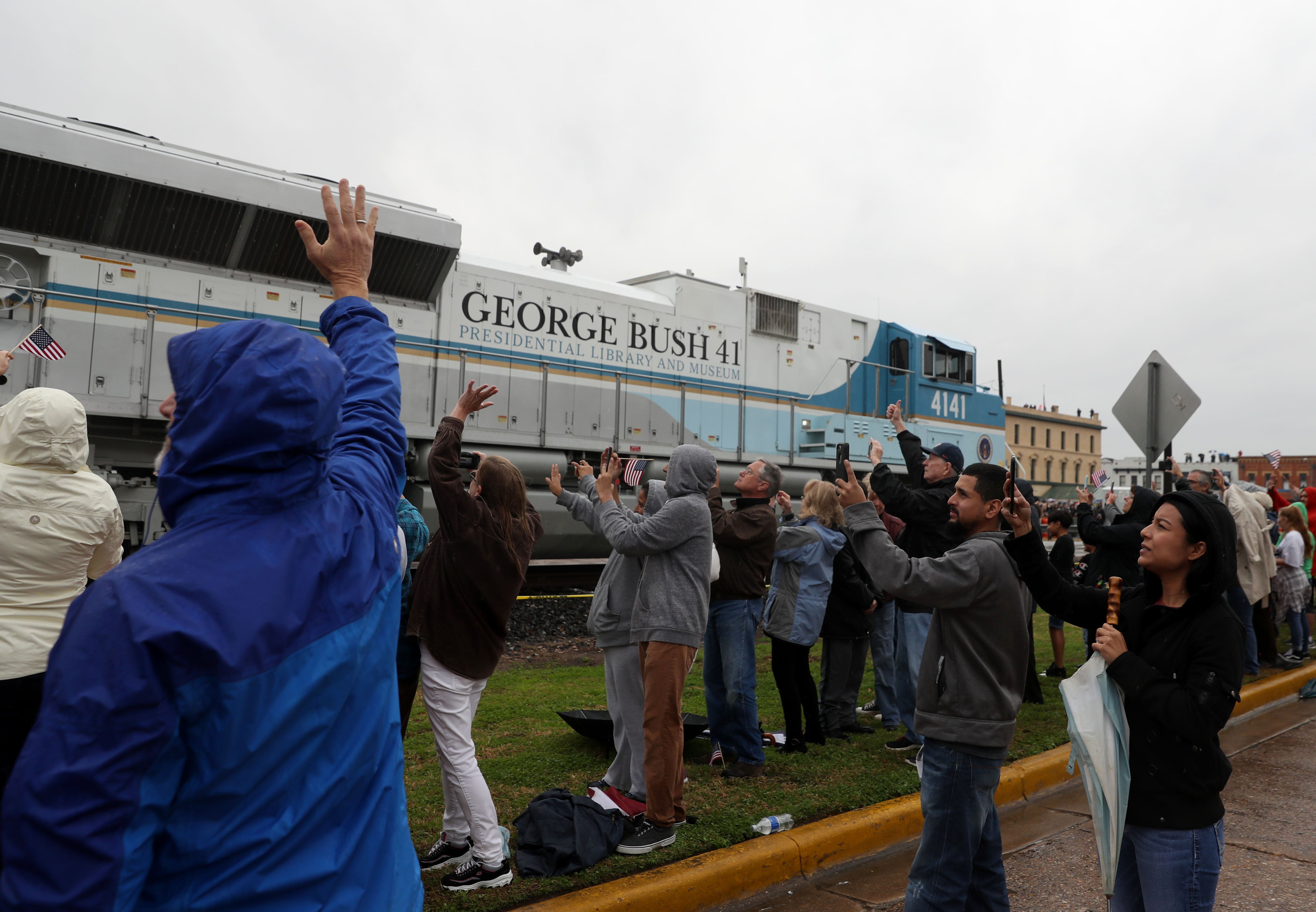 People wave at a train that is carrying the casket of former U.S. President George H.W. Bush to the George H.W. Bush Presidential Library at Texas A&M University on 6 December, 2018 in Navasota, Texas