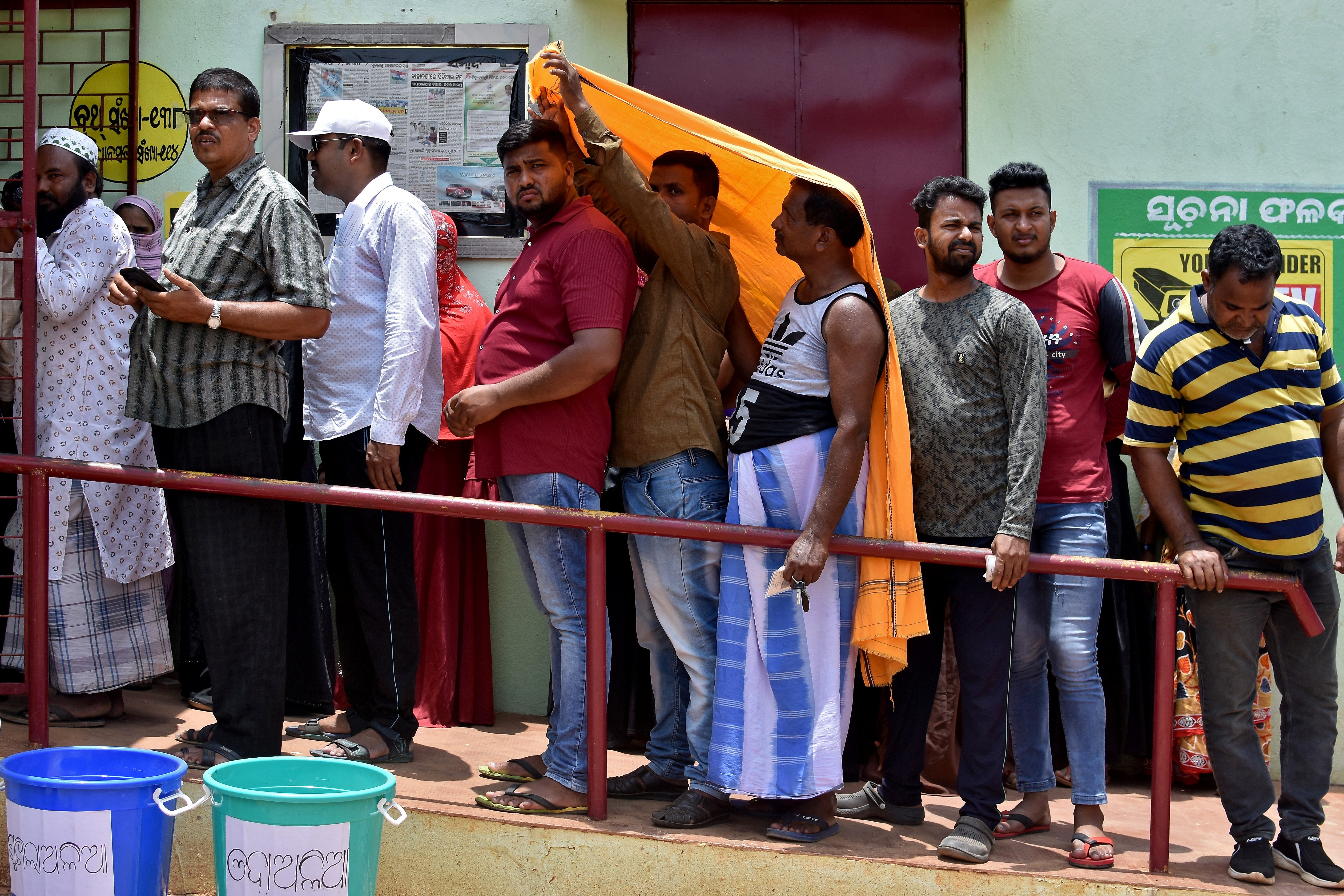 Men use a stole to cover from heat as they wait in a line outside a polling station to cast their votes during the sixth phase of India's general election, on a hot summer day in Bhubaneswar, India