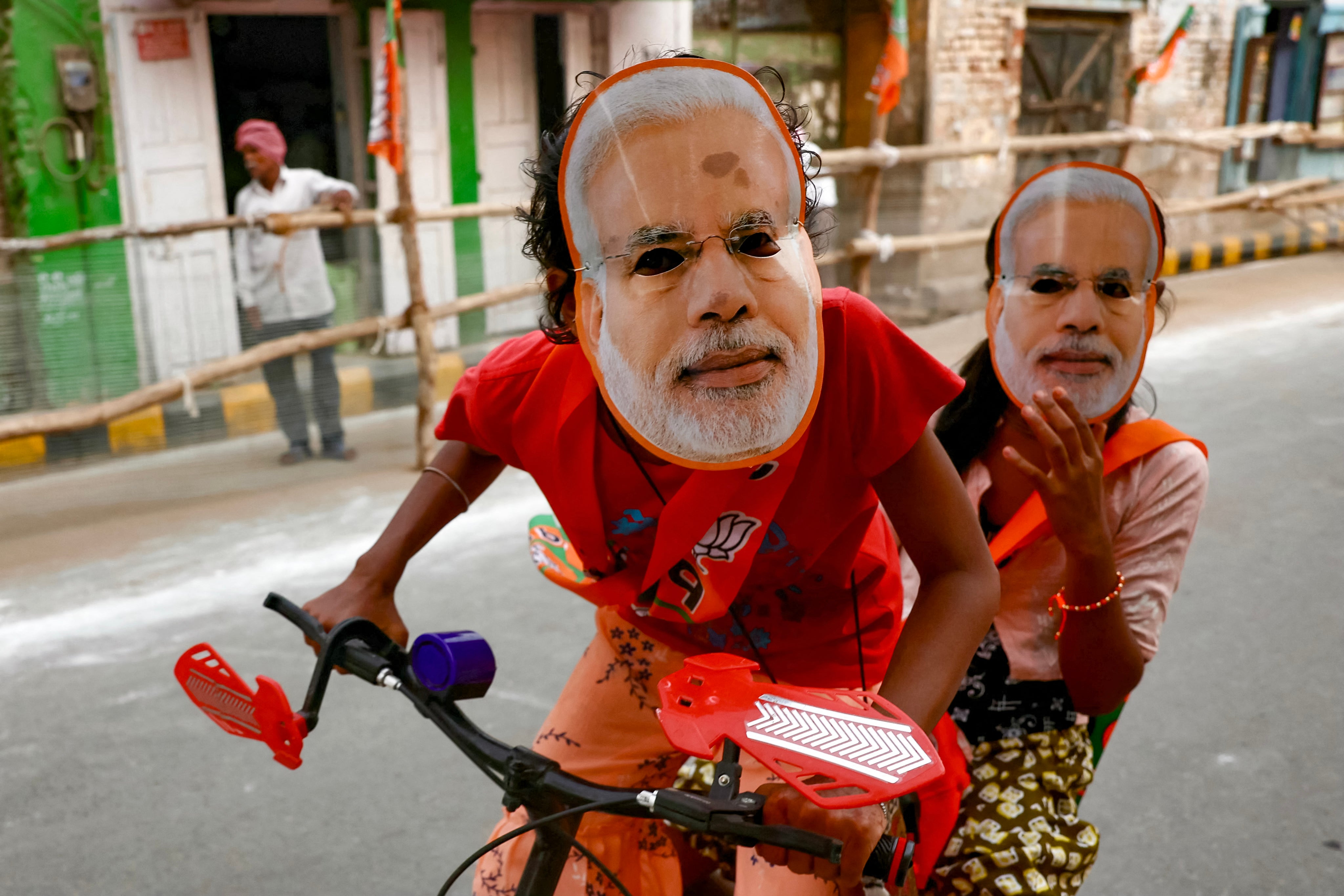 Children riding a bicycle wear masks portraying Narendra Modi in Varanasi