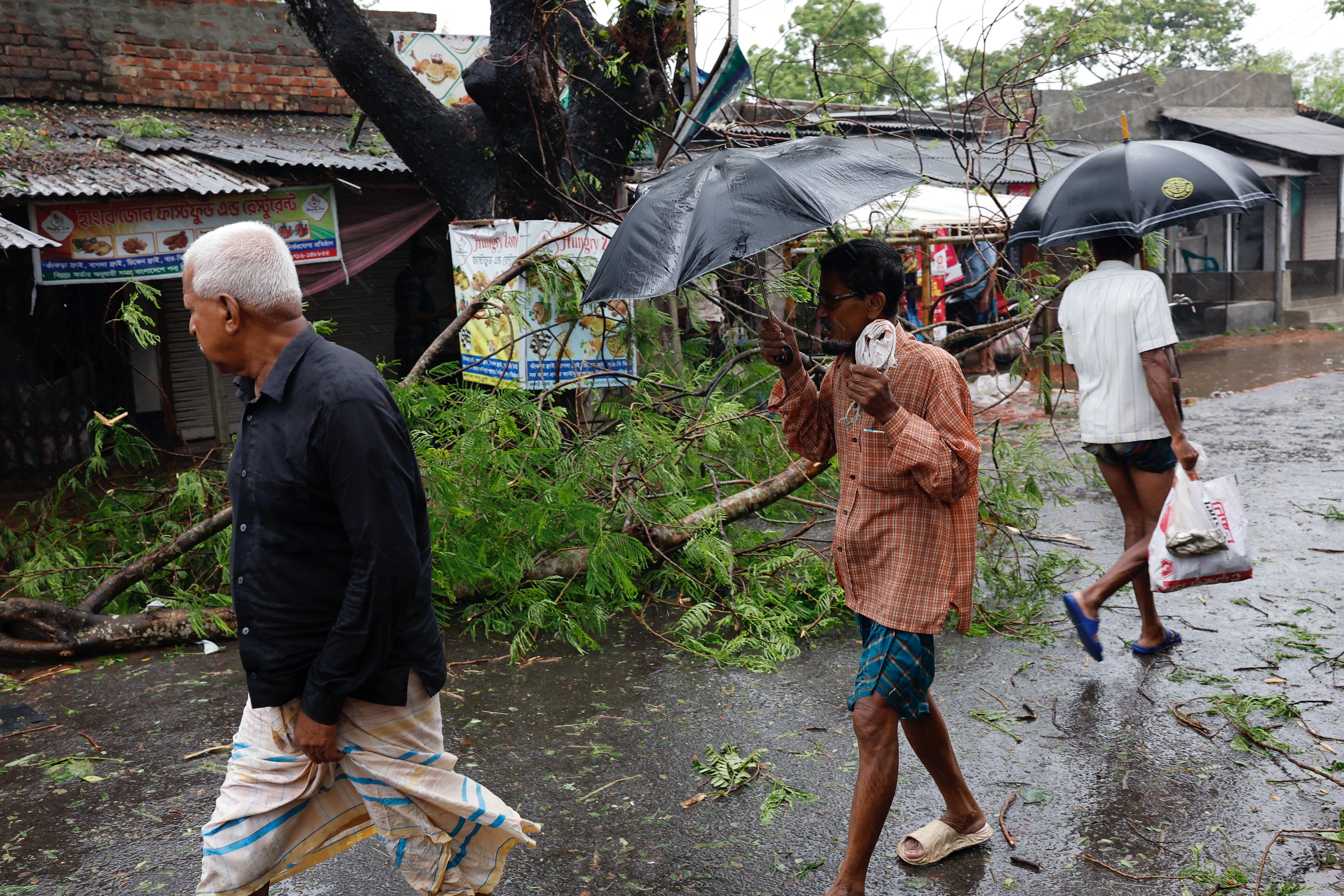 People walk past a fallen tree branch as Cyclone Remal hits the country, in the Shyamnagar area of Satkhira