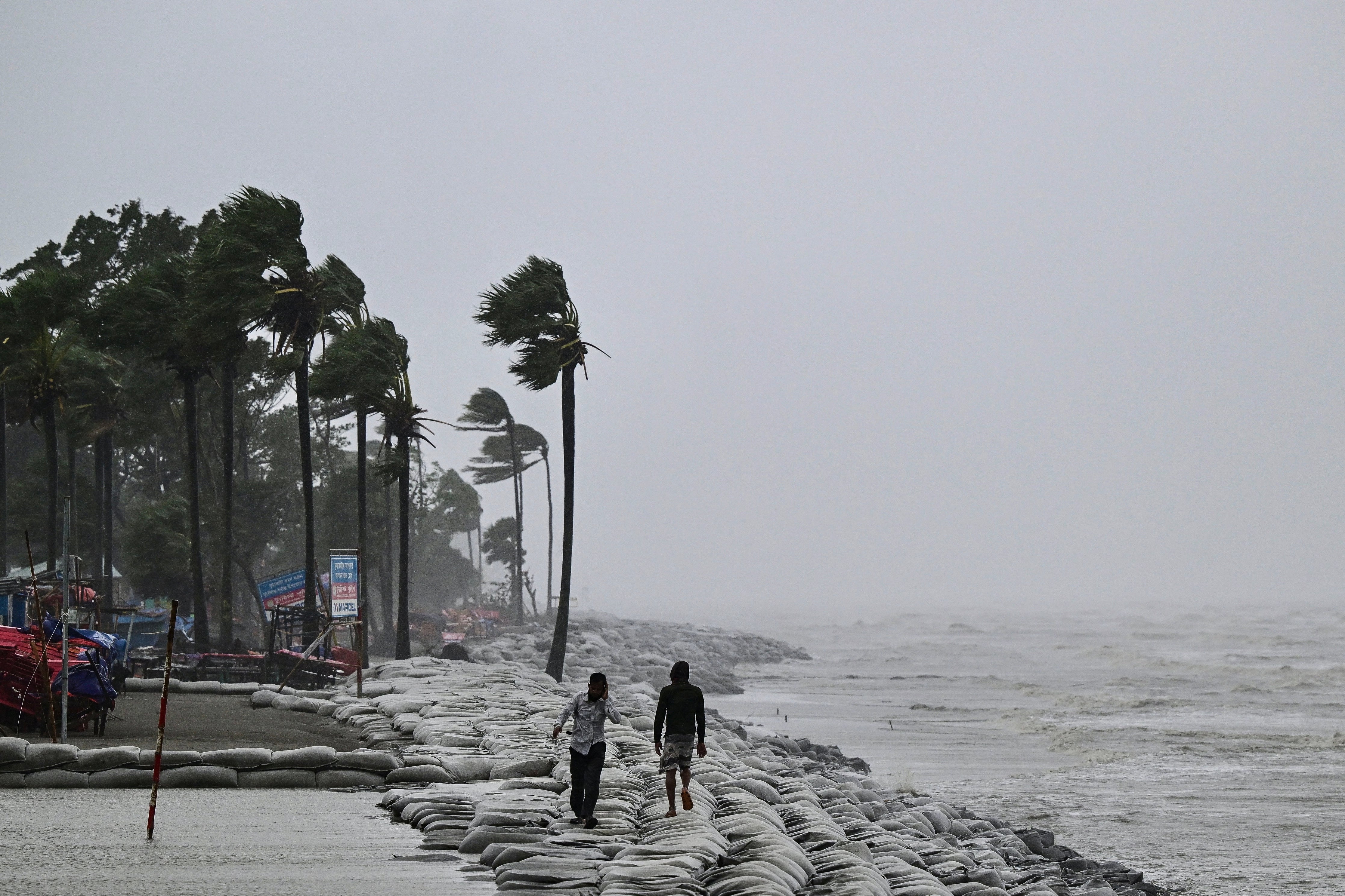 People walk along a beach during rainfall following the landfall of Cyclone Remal in Kuakata on 27 May 2024
