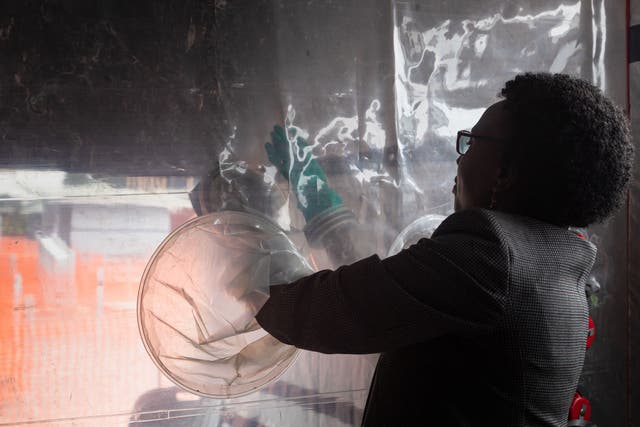 <p>Uganda’s Health Minister Jane Ruth Aceng tries to use the gloves through the transparent medical intervention wall at the newly installed makeshift Ebola Treatment Unit with 32 beds, also to be used as a research centre for Ebola strains and vaccine trial, in Kampala on December 9, 2022</p>