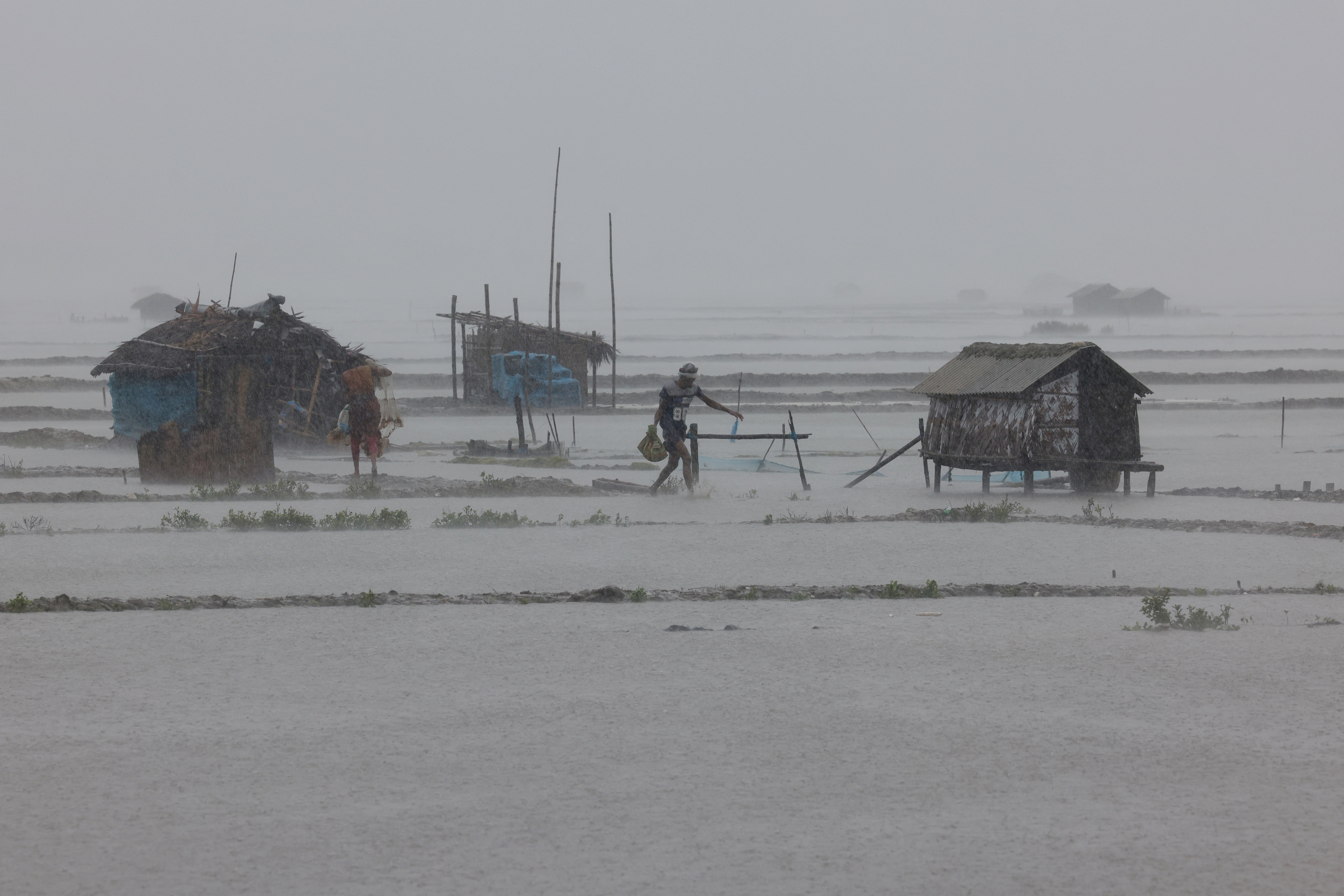 People walk along shrimp and crab farms that are flooded due to heavy rain as Cyclone Remal passes the country, in the Shyamnagar area of Satkhira, Bangladesh