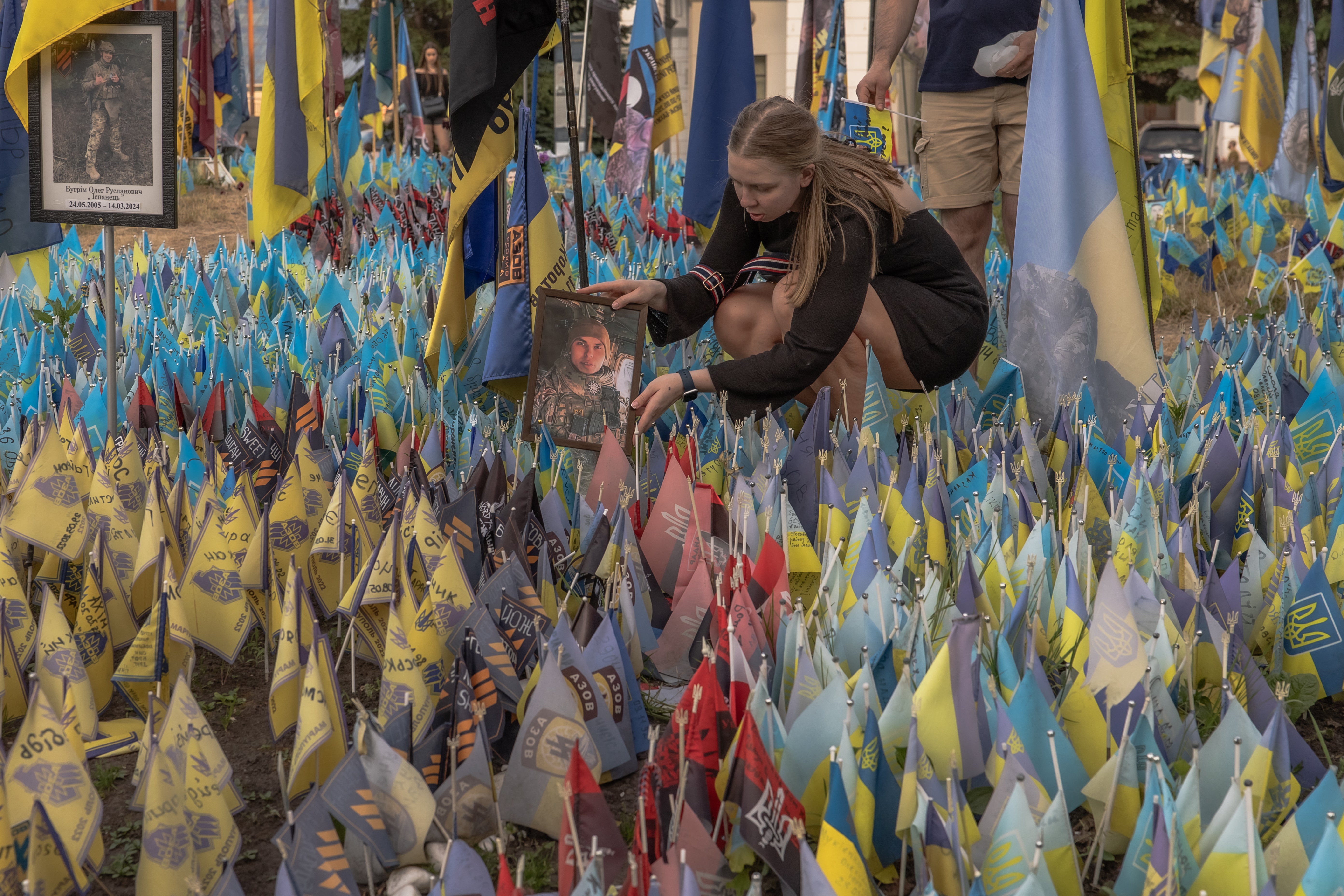 A woman displays a portrait of a Ukrainian army serviceman at a memorial area with Ukrainian and other countries flags commemorating fallen Ukrainian and foreign fighters at the Independence Square, in Kyiv
