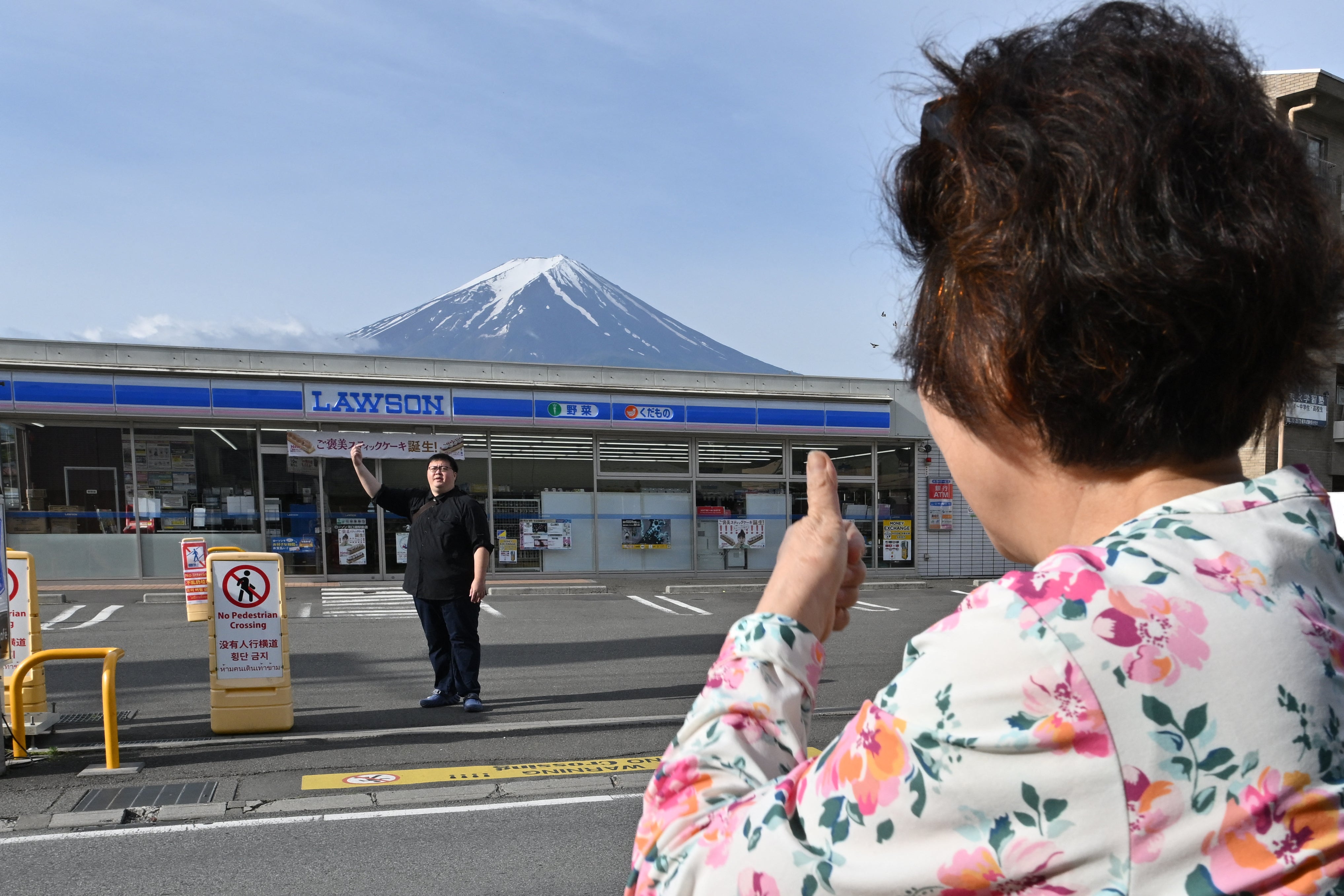 Uma pessoa tira fotos do Monte Fuji do outro lado da rua de uma loja de conveniência, horas antes da instalação de uma barreira