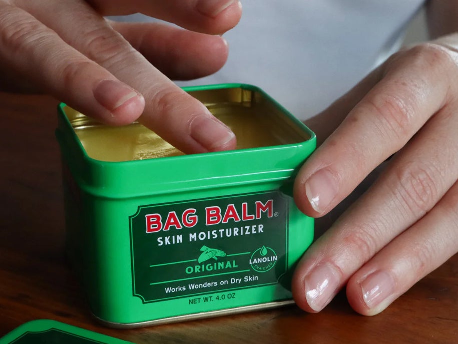 A hand dips into a can of Vermont Original Bag Balm skin moisturizer.
