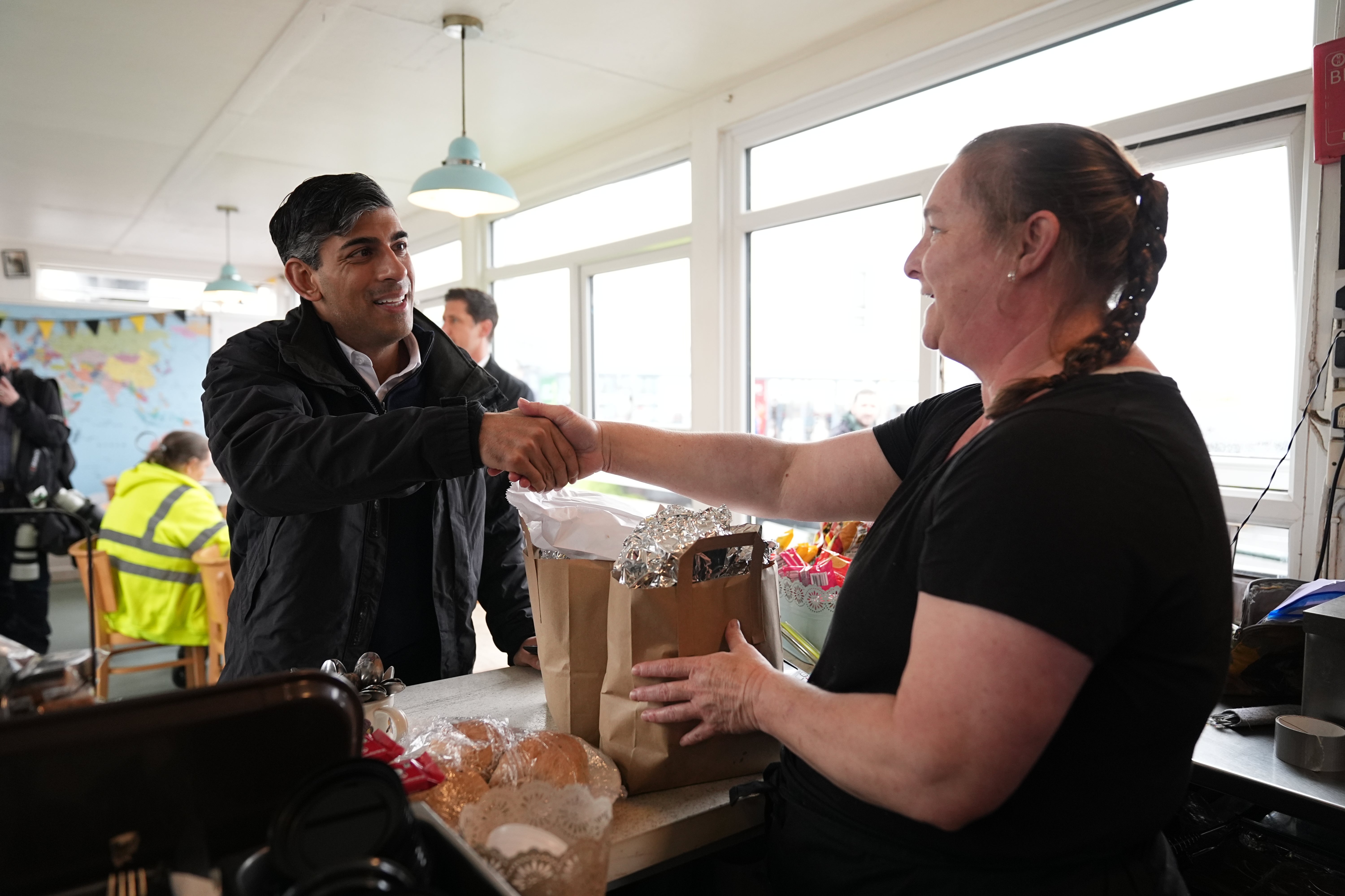 Prime Minister Rishi Sunak shakes hands with a cafe worker as he picks up breakfast for the media in Cornwall,