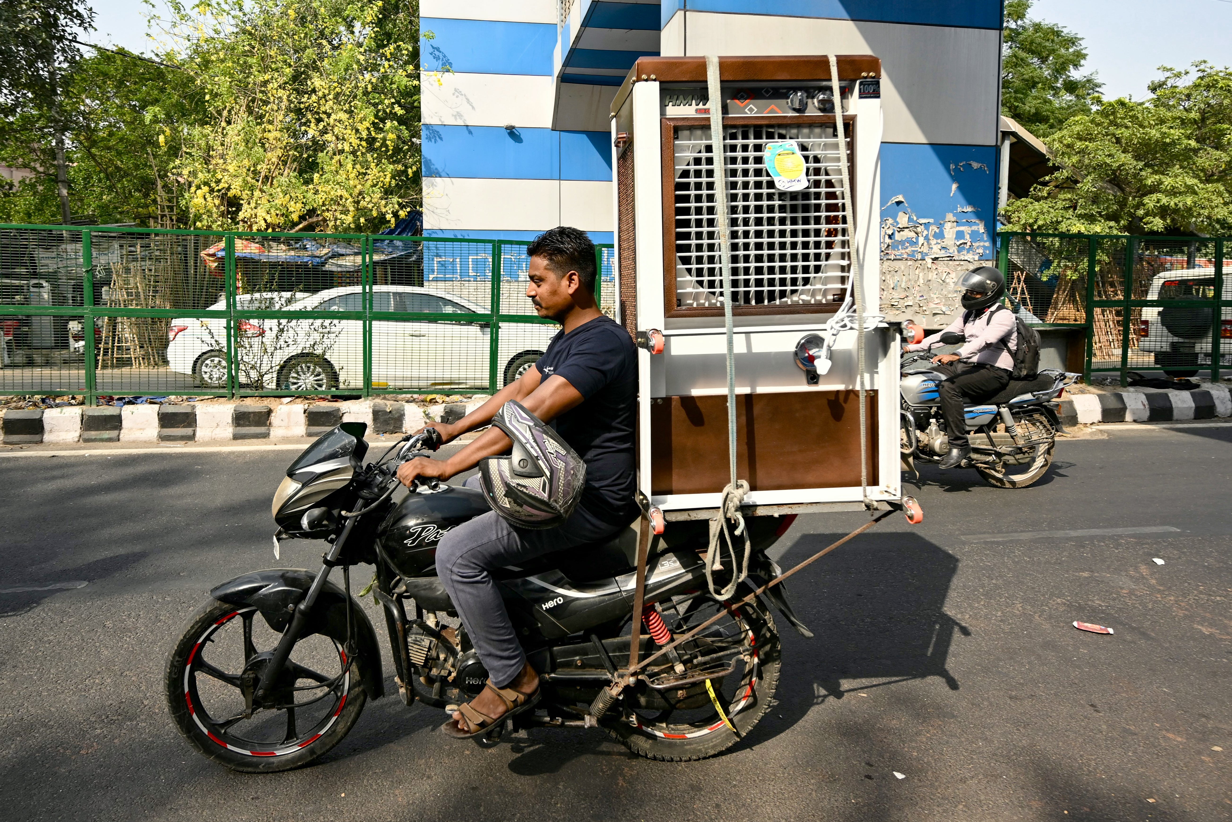 A man carrying a newly purchased air cooler rides a bike along a street, on a hot summer afternoon in Delhi