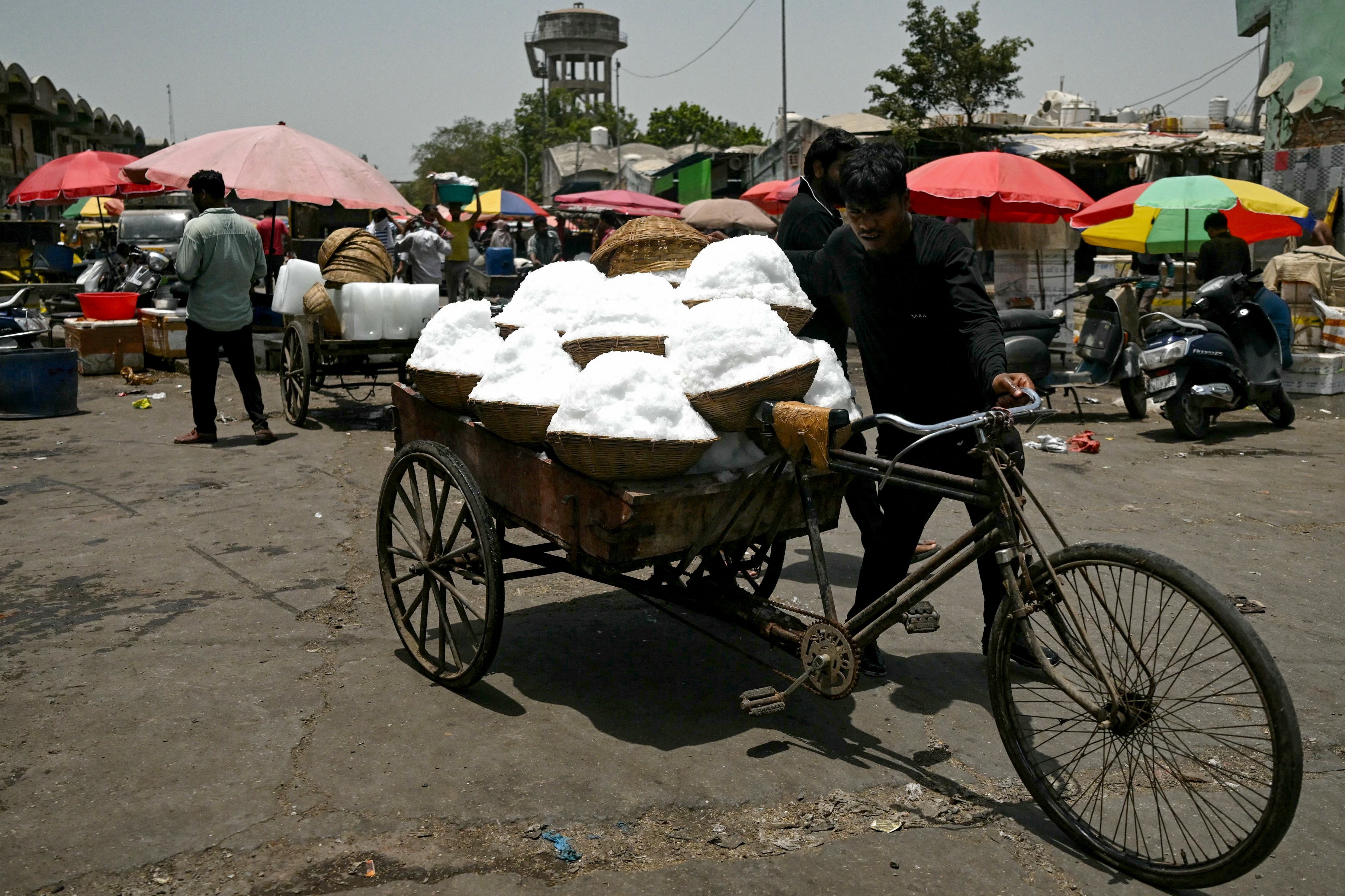 A worker carries baskets of shaved ice to a food processing unit on a hot summer afternoon, at a market in Delhi