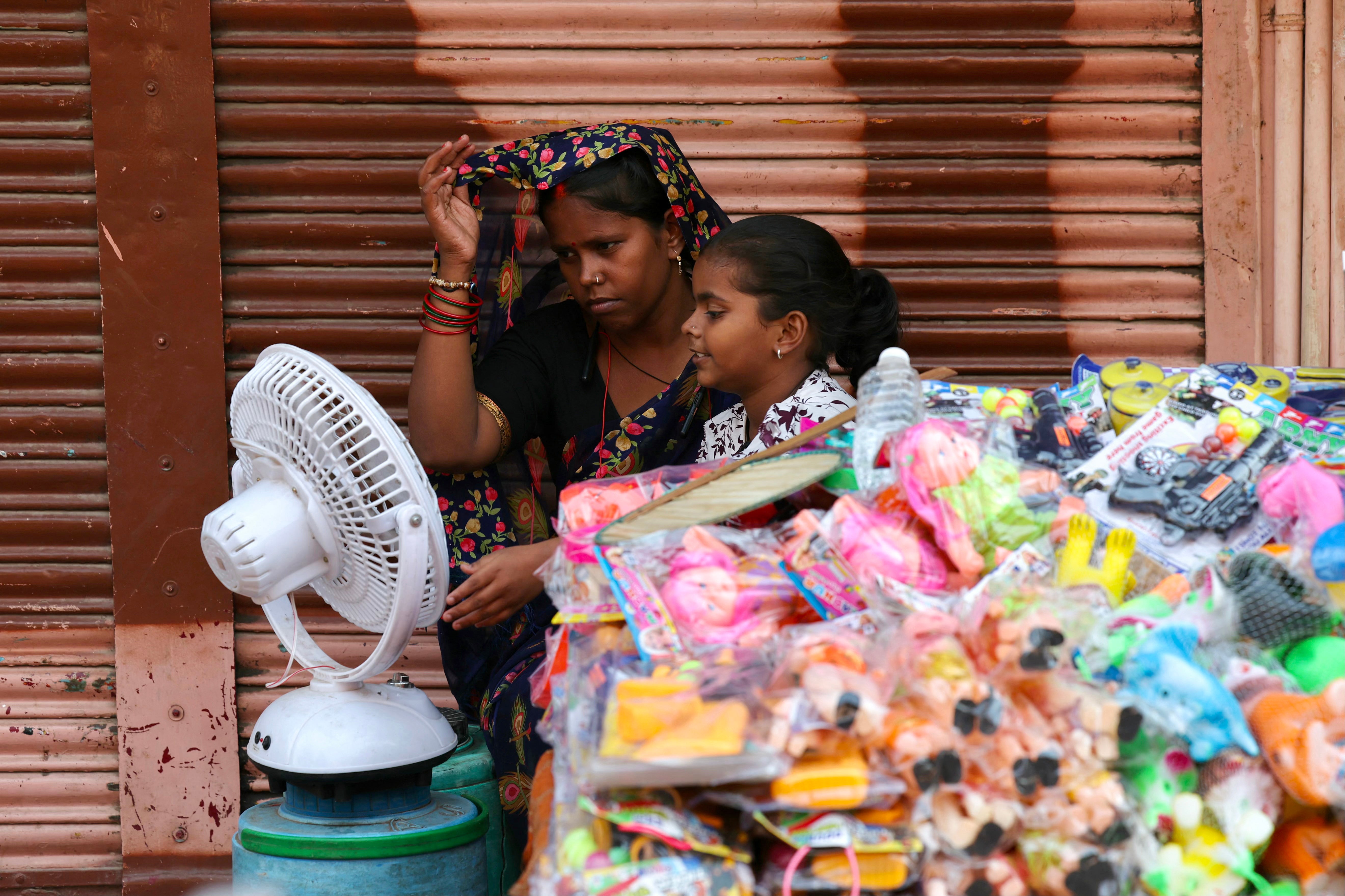 People sit in front of a table fan to cool off on a hot summer afternoon in Varanasi
