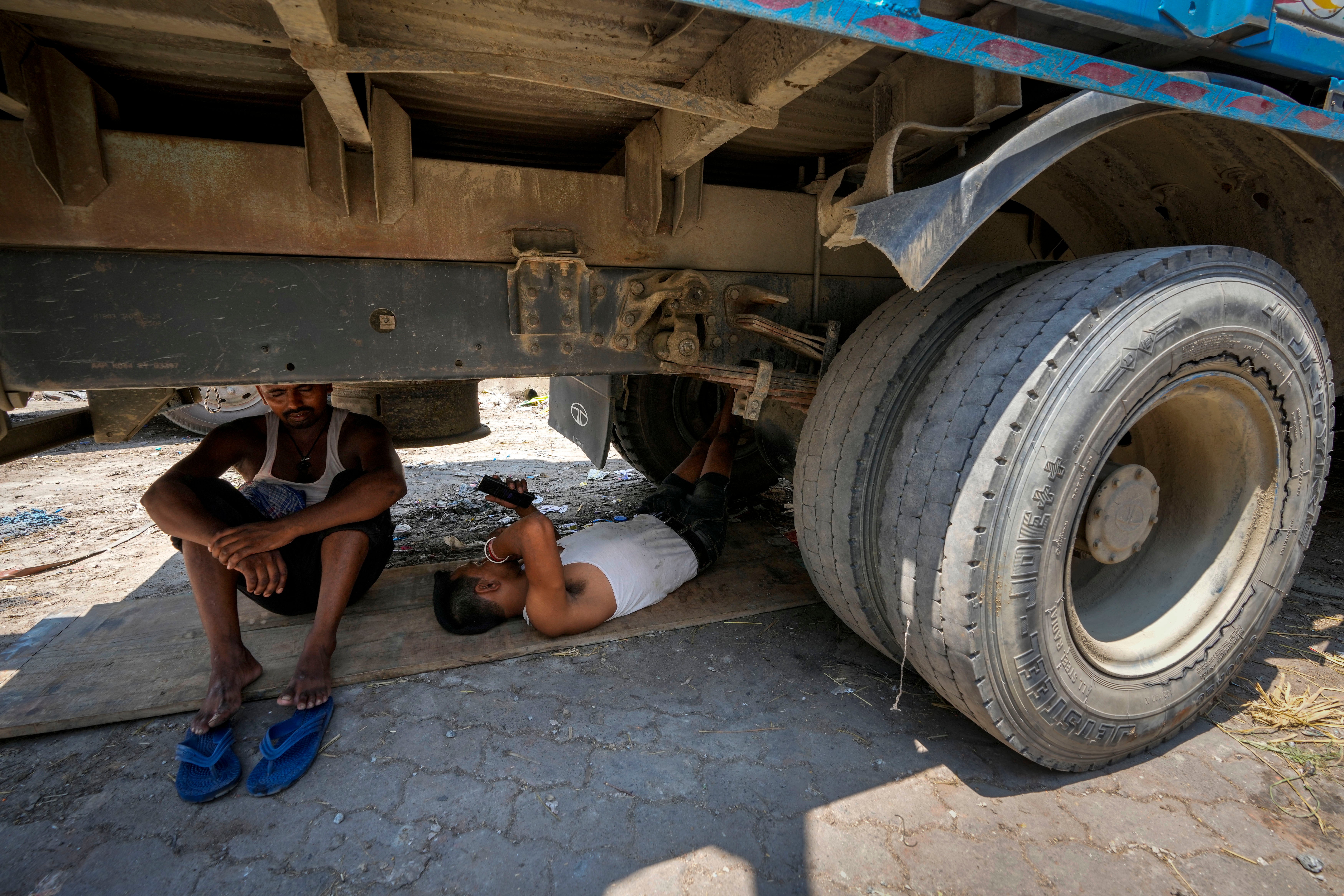 Workers take refuge beneath a parked truck from the scorching heat, in Guwahati, India