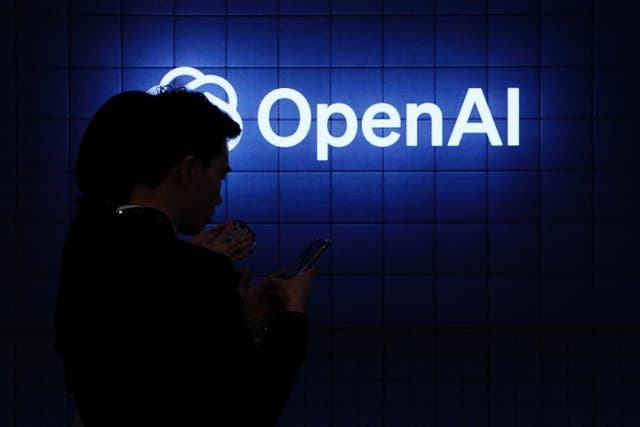 Visitor look at their phone next to an Open AI’s logo during the Mobile World Congress (MWC), the telecom industry’s biggest annual gathering, in Barcelona on February 26, 2024