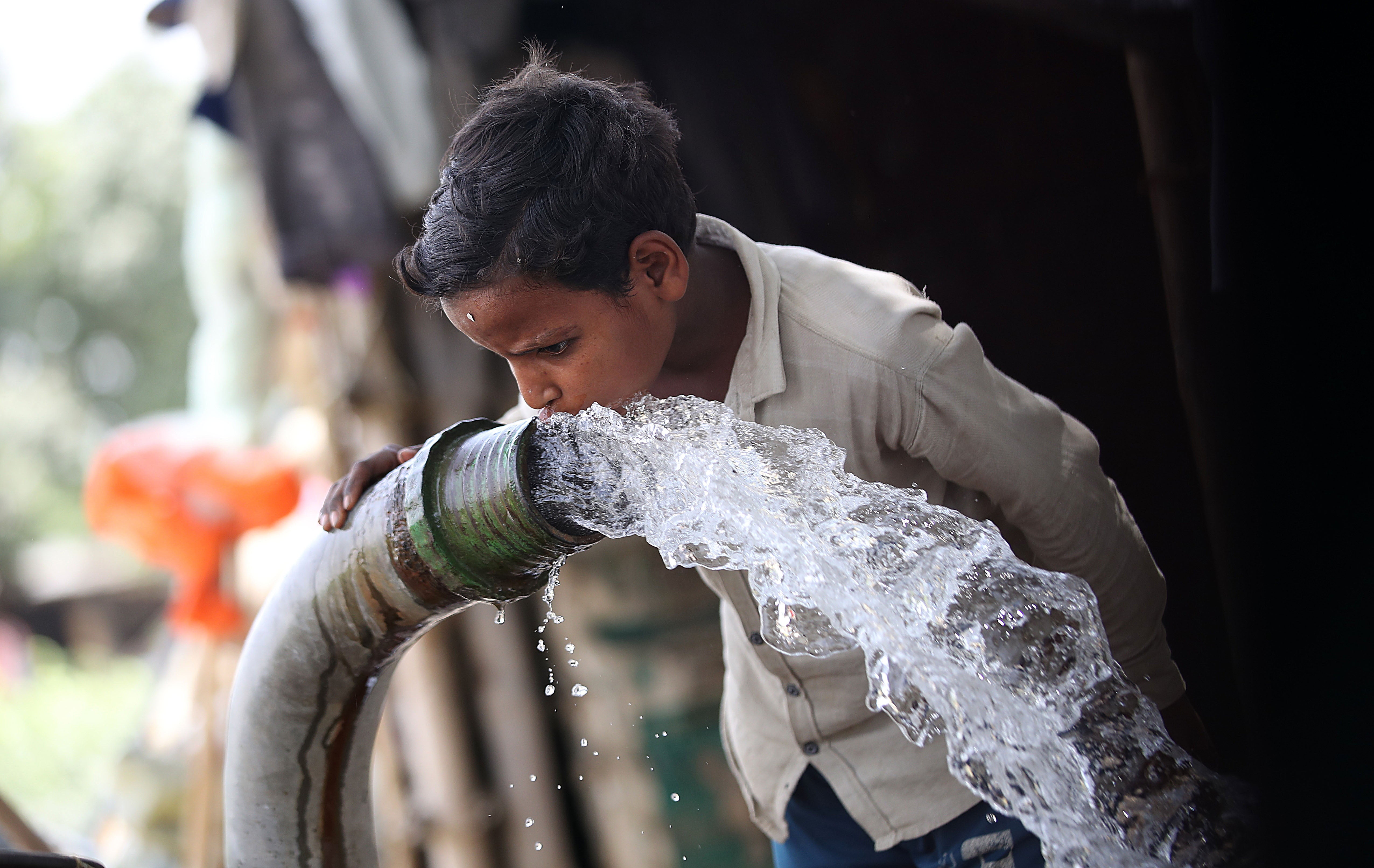 A boy drinks water to cool himself in a tubewell on a hot day at the fields in New Delhi, India, 31 May 2024