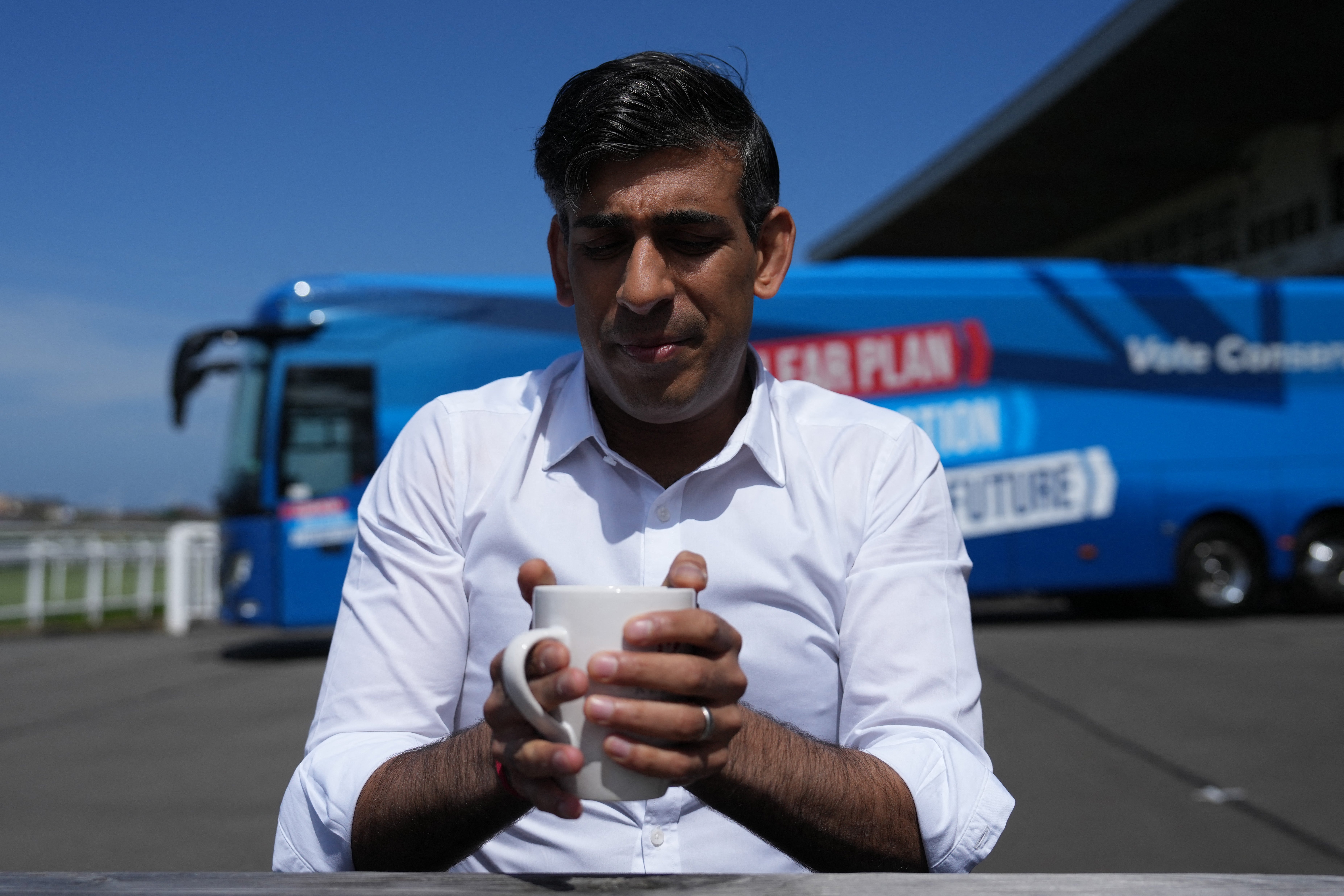 Britain's Prime Minister and Conservative Party leader Rishi Sunak holds a mug while speaking to journalists at Redcar racecourse