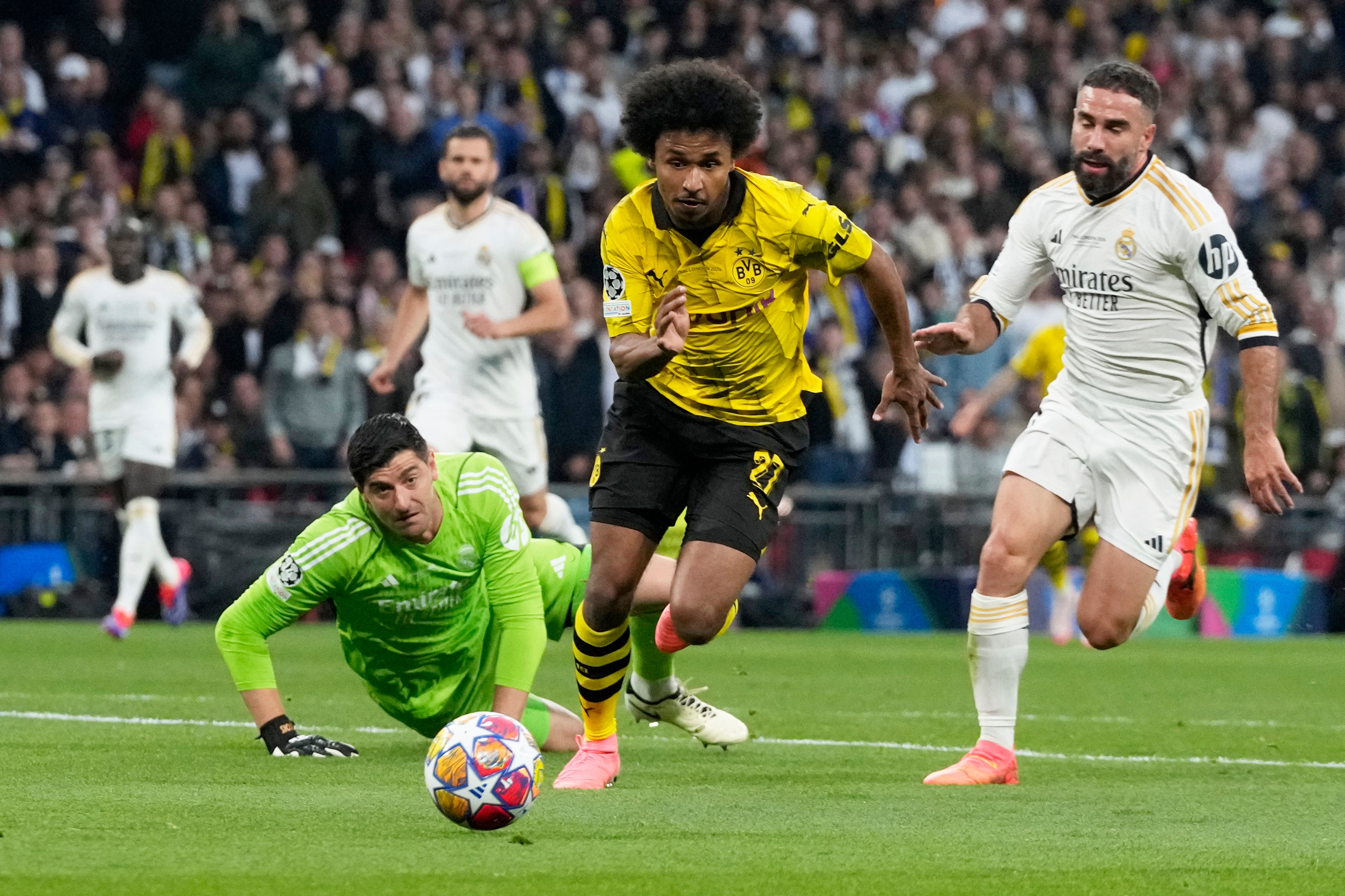Dortmund's Karim Adeyemi, center, gets past Real Madrid's goalkeeper Thibaut Courtois, on the ground