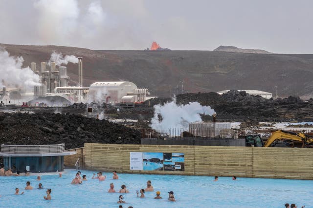 <p>The Blue Lagoon with people bathing in it as the volcanic crater spews lava in the background in Grindavik</p>