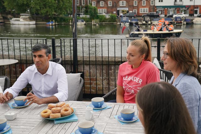 Rishi Sunak and the parliamentary candidate for Henley Caroline Newton (far right) speaking to rowing club members while Liberal Democrat supporters pass by on a boat, during a visit to the Leander Club in Henley-on-Thames, Oxfordshire (Jonathan Brady/PA)