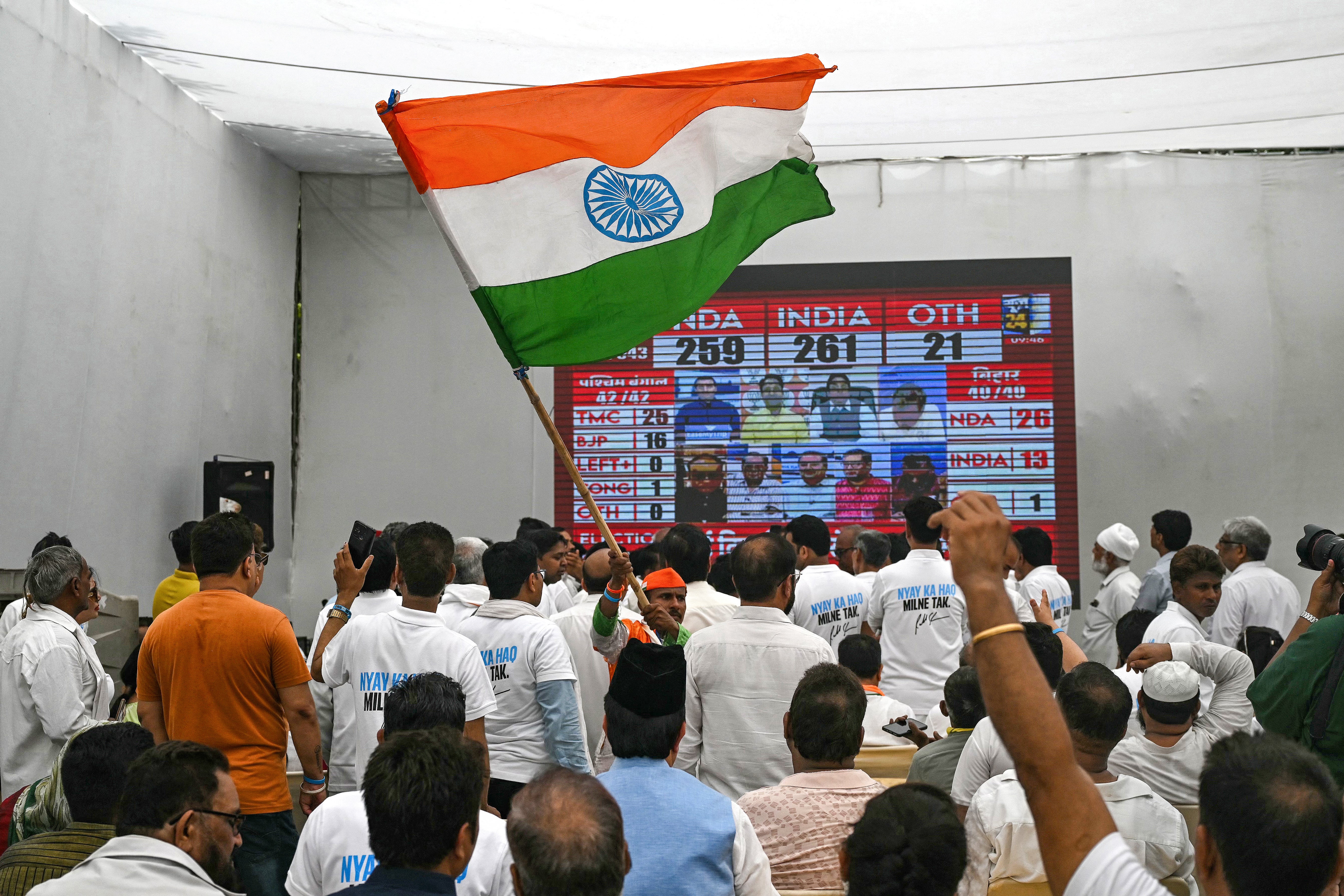 A supporter of the Indian National Congress party waves India’s national flag as others watch live election results displayed on a television