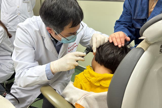 <p>Dr Yilai Shu examining a young patient</p>