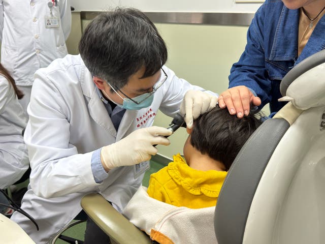 <p>Dr Yilai Shu examining a young patient</p>