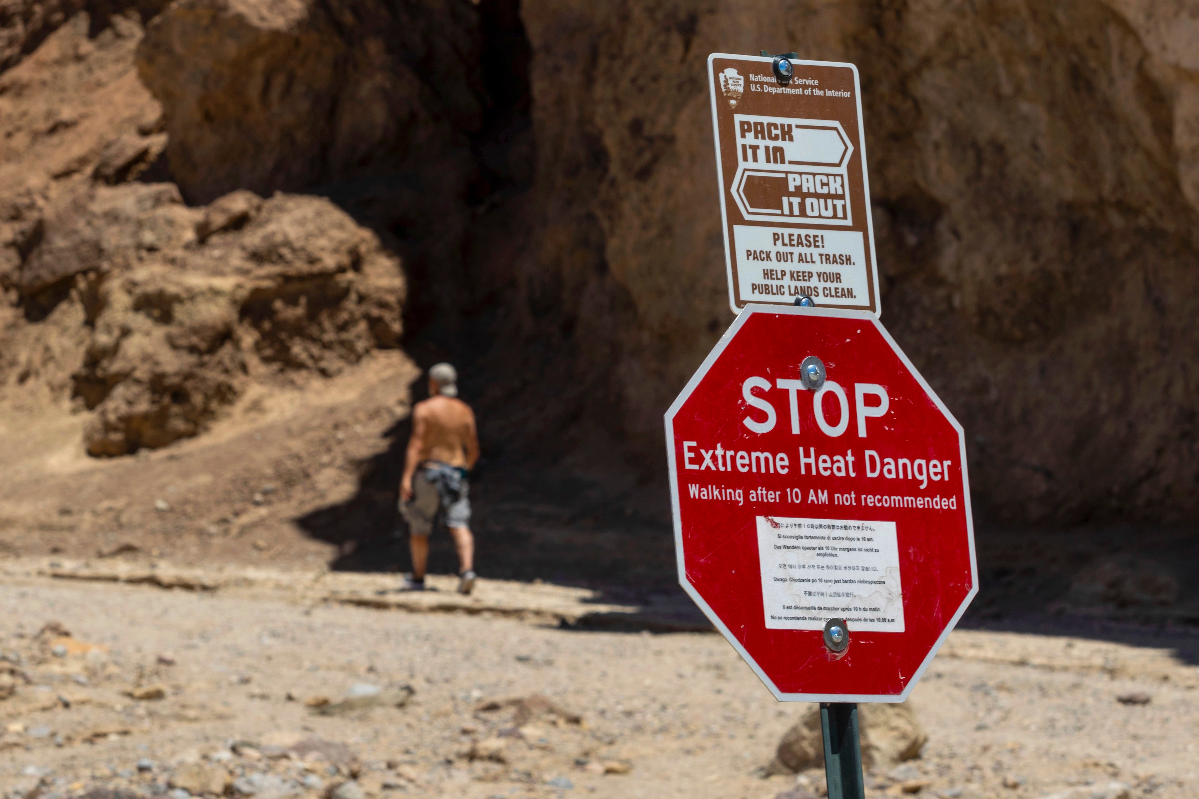 A hiker passes a sign warning of extreme heat at the start of the Golden Canyon trail, in Death Valley National Park, where a motorcylist died from extreme heat on July 6