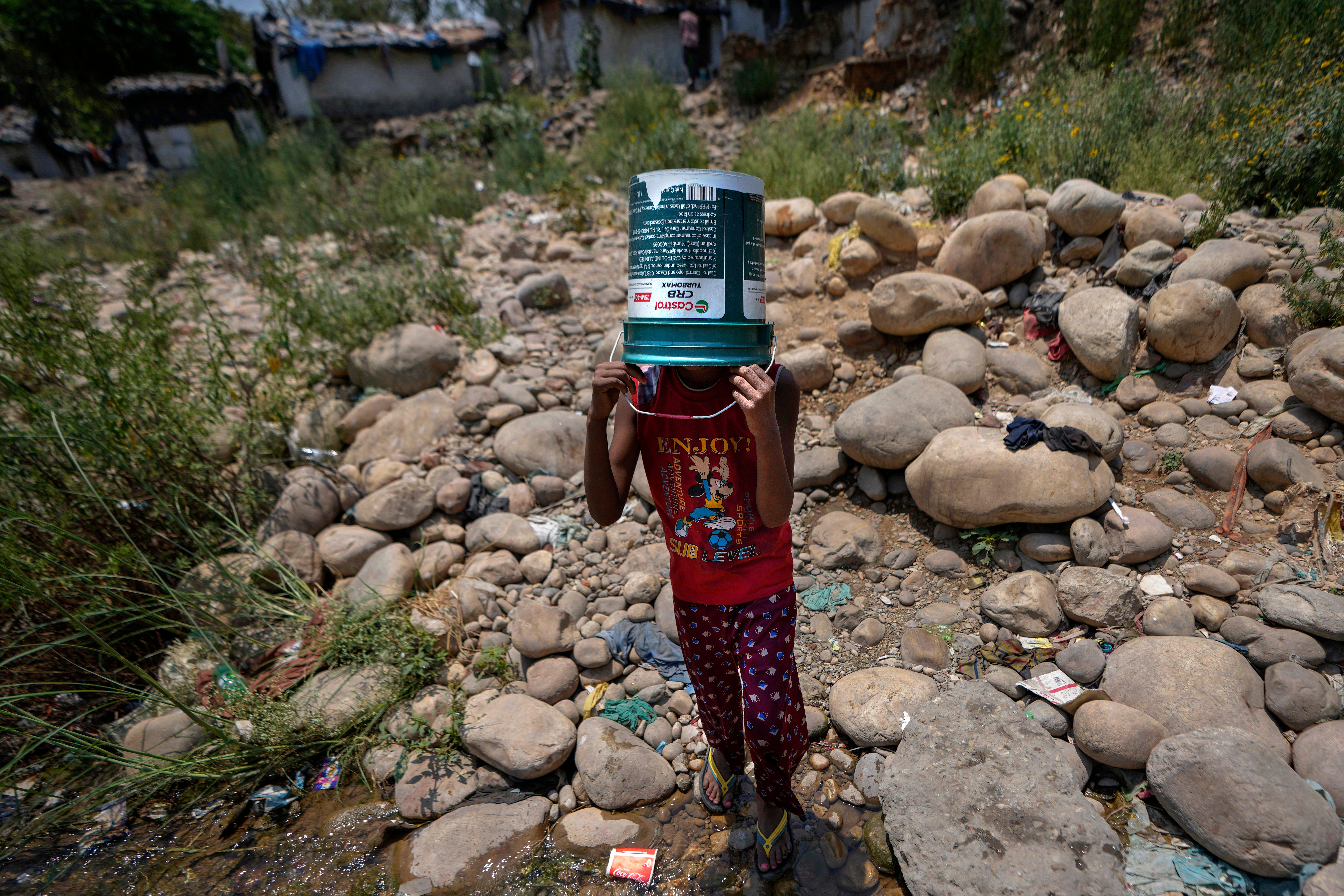 <p>Girl shields herself from the sun as she walks to collect water from a leaking municipal pipe on a hot summer day on the outskirts of Jammu city, India</p>