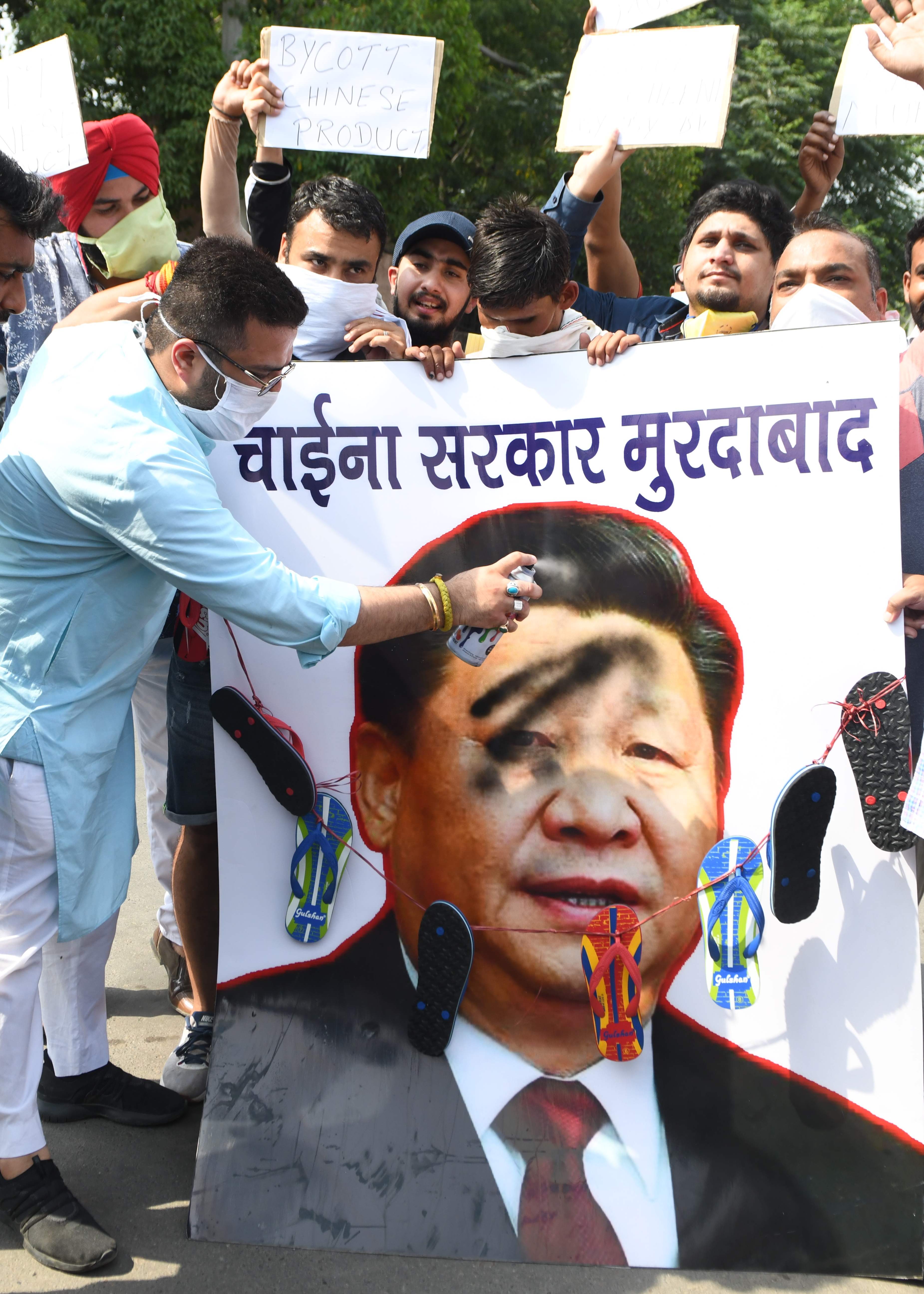 Activists of the ruling Bharatiya Janata Party spray black paint on a poster depicting Chinese President Xi Jinping during a protest against China