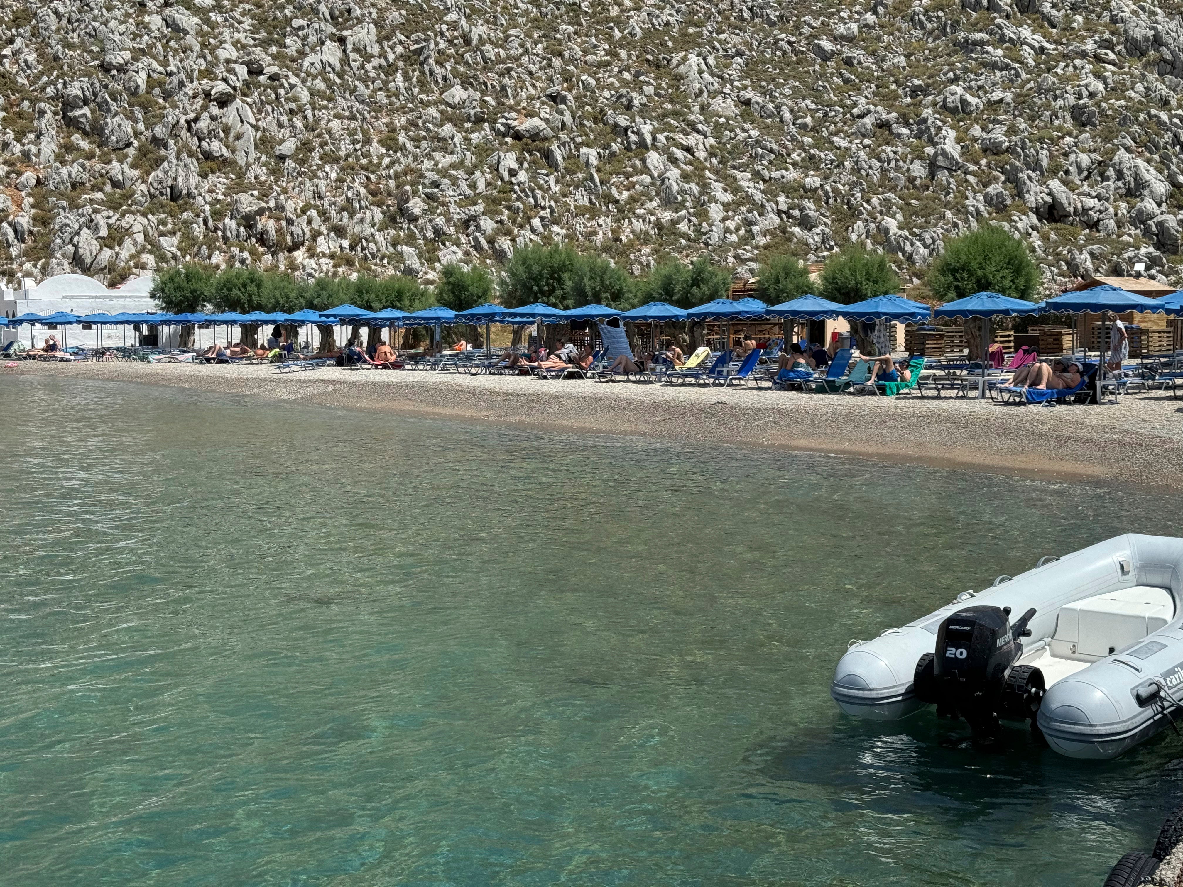People sit on the beach of Agios Nikolaos from where British doctor and television presenter Michael Mosley, is believed to have set out, on the southeastern Aegean Sea island of Symi, Greece