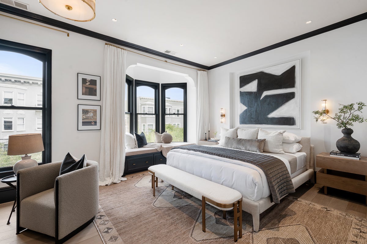 Principal bedroom of the iconic home. The walls are painted largely white or light gray, with most rooms punctuated with splashes of color on door frames, the fireplace mantle, and cabinets