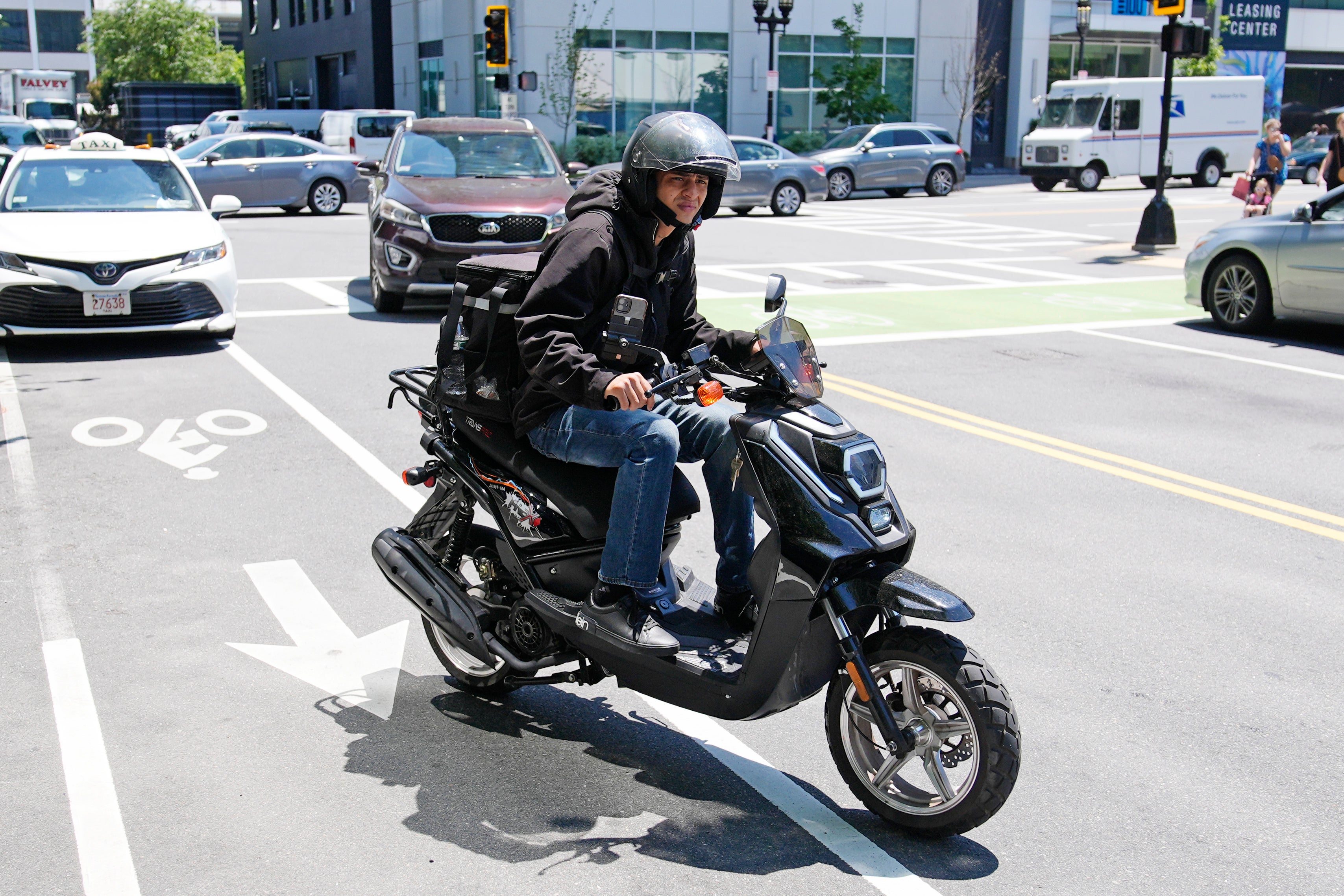 A delivery driver on a scooter heads to a delivery in the Seaport district, Friday, June 7, 2024, in Boston.