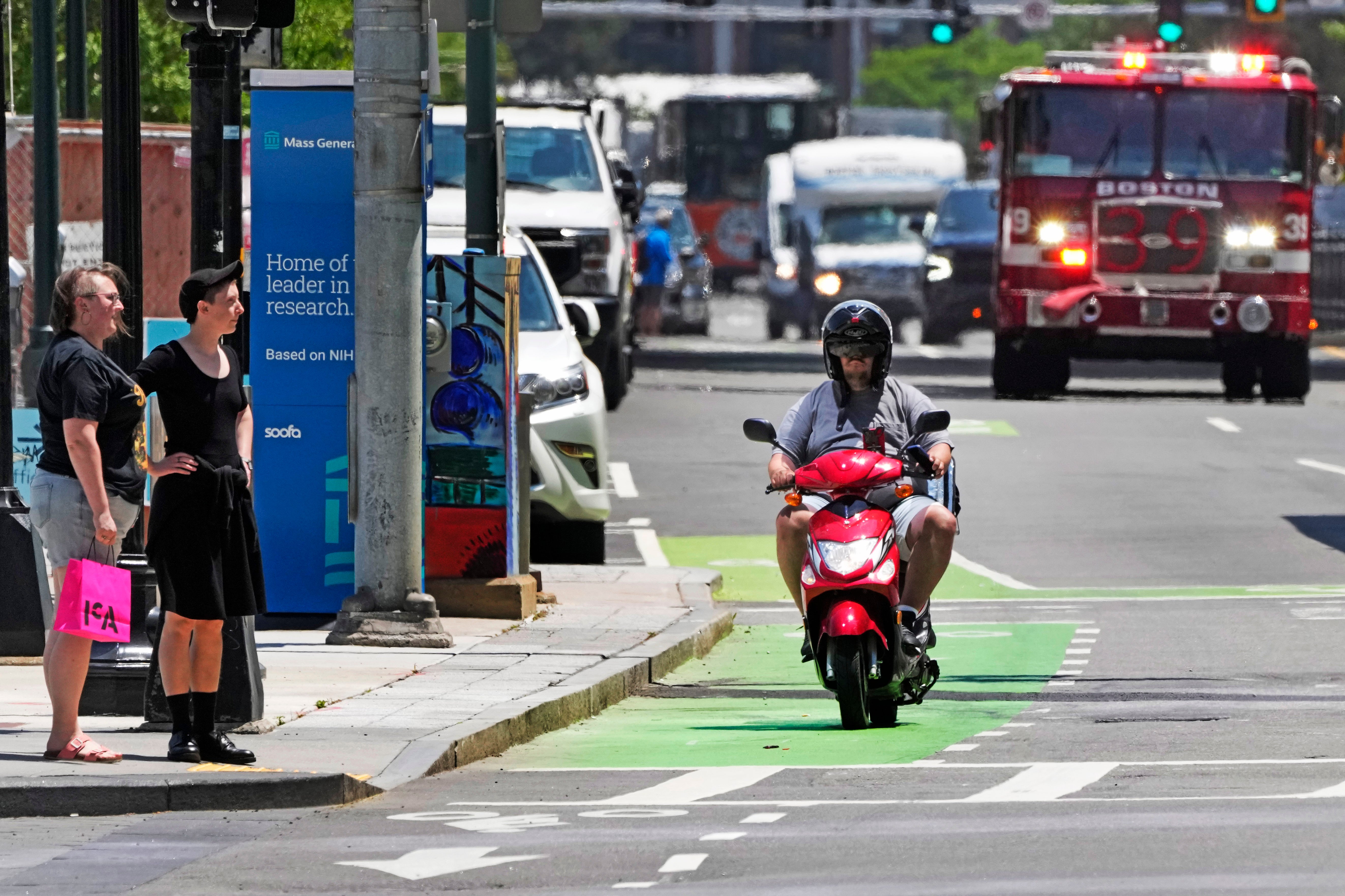 A delivery driver on a scooter keeps pace with a fire engine on a call in the Seaport District, Friday, June 7, 2024