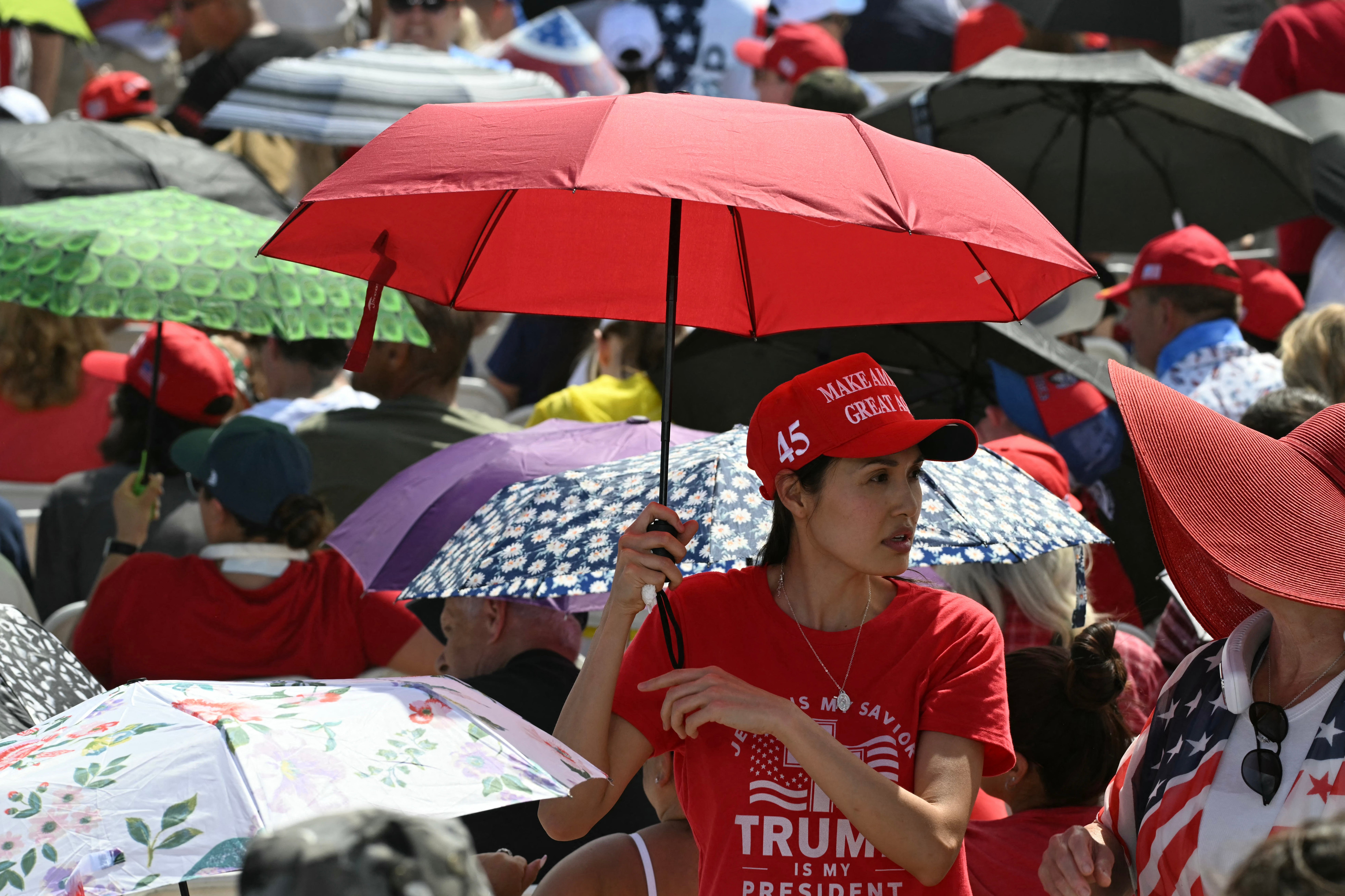 MAGA supporters protect themselves from the sun as they wait for Trump to appear at a rally in Las Vegas