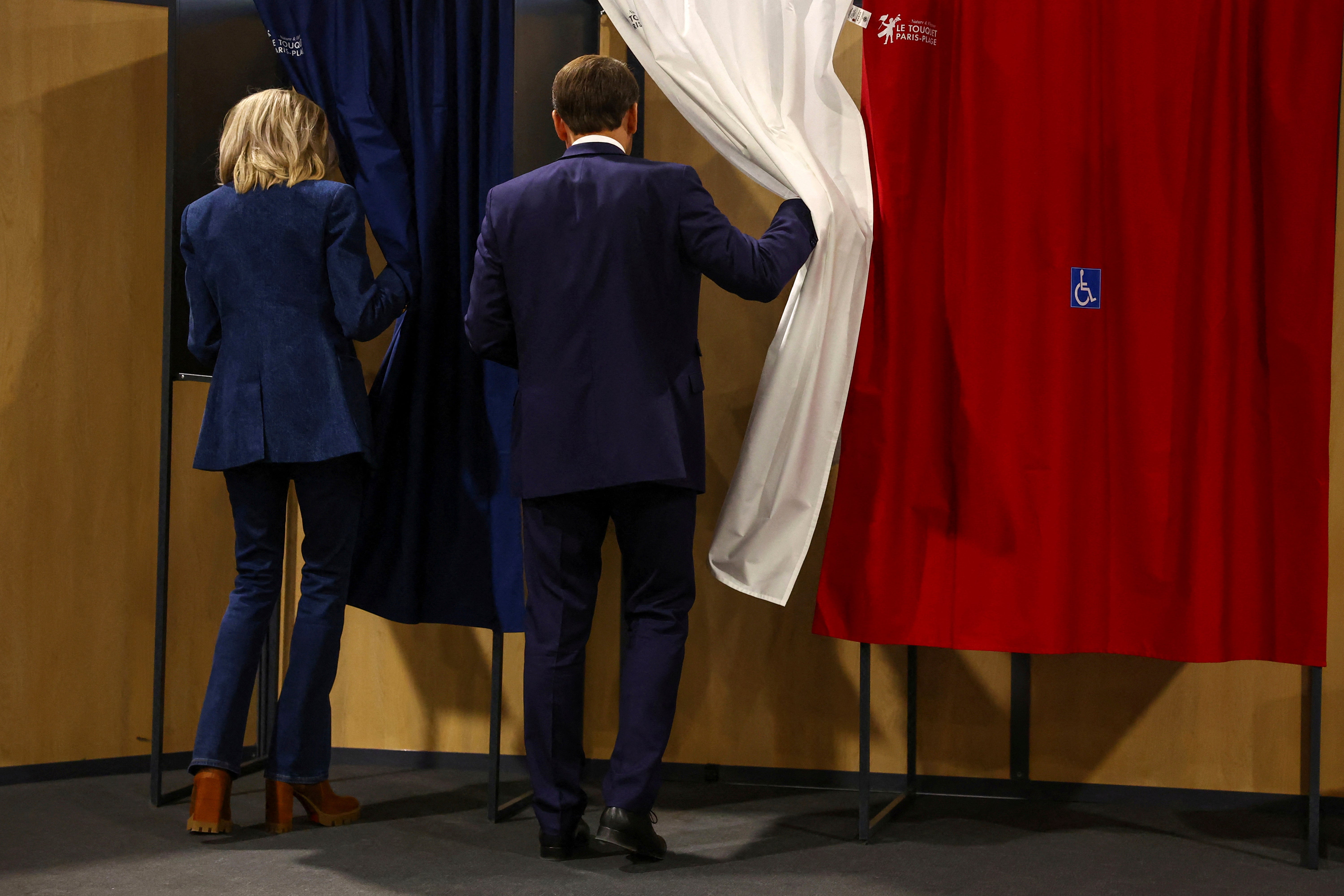 French President Emmanuel Macron and his wife Brigitte Macron enter a voting booth during the European elections on Sunday