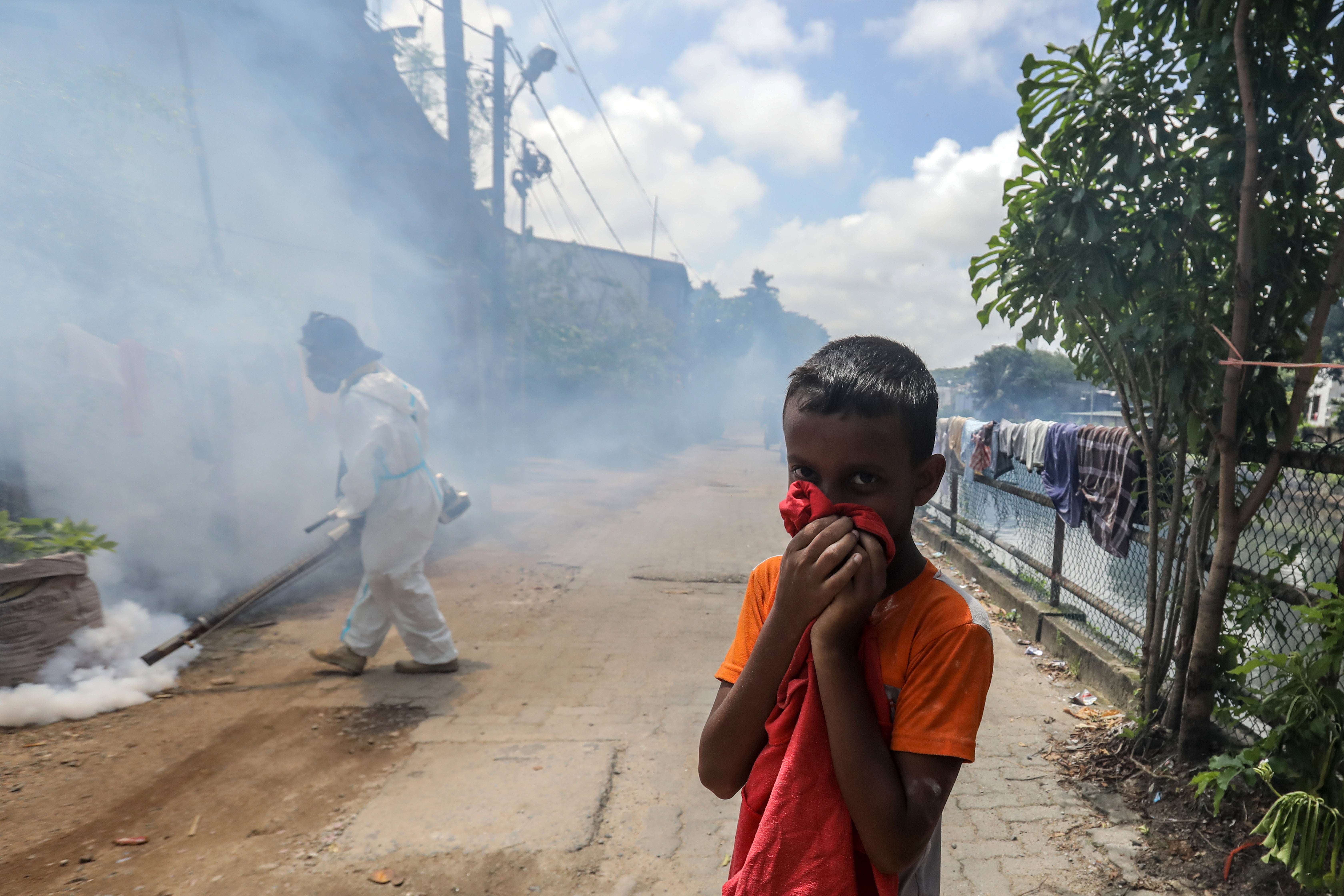 A boy covers his mouth as a Sri Lankan health worker fumigates insecticide to curb mosquito breeding in an attempt to control dengue fever in Colombo, Sri Lanka