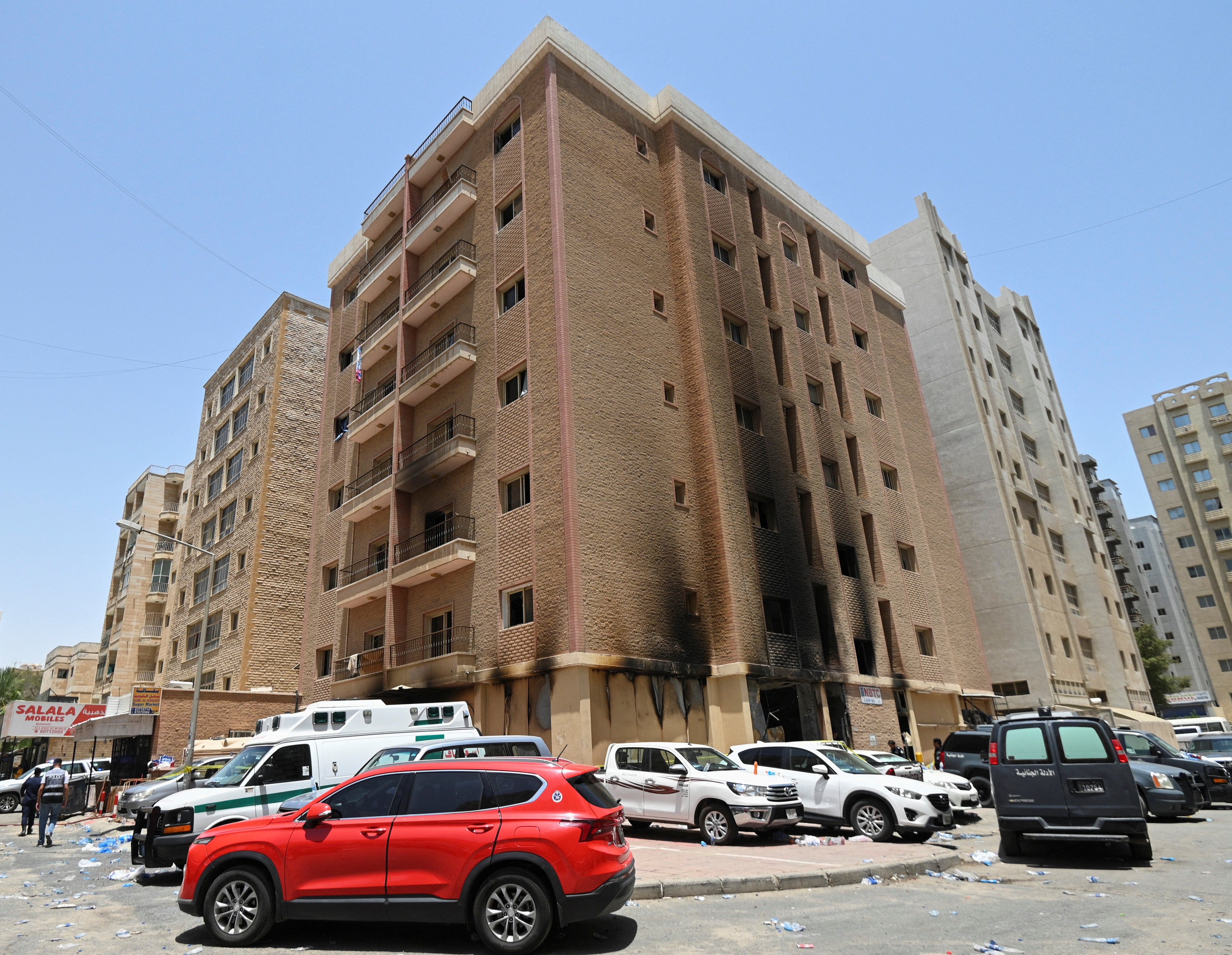 Vehicles are parked next to a building damaged following a deadly fire, in Mangaf, southern Kuwait