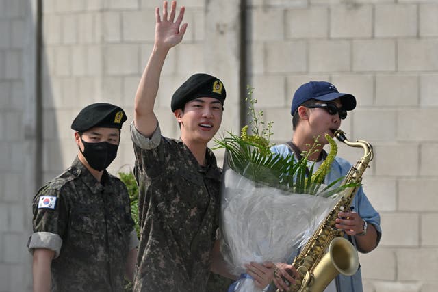 <p>K-pop boy band BTS member Jin (C) waves after being discharged from his mandatory military service next to fellow BTS members RM (R) and Jimin (L) outside a military base in Yeoncheon on 12 June, 2024</p>