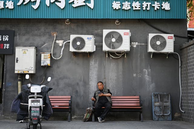 <p>A man sits beneath air conditioning units in Beijing. A record-breaking heatwave has been broiling parts of Asia</p>